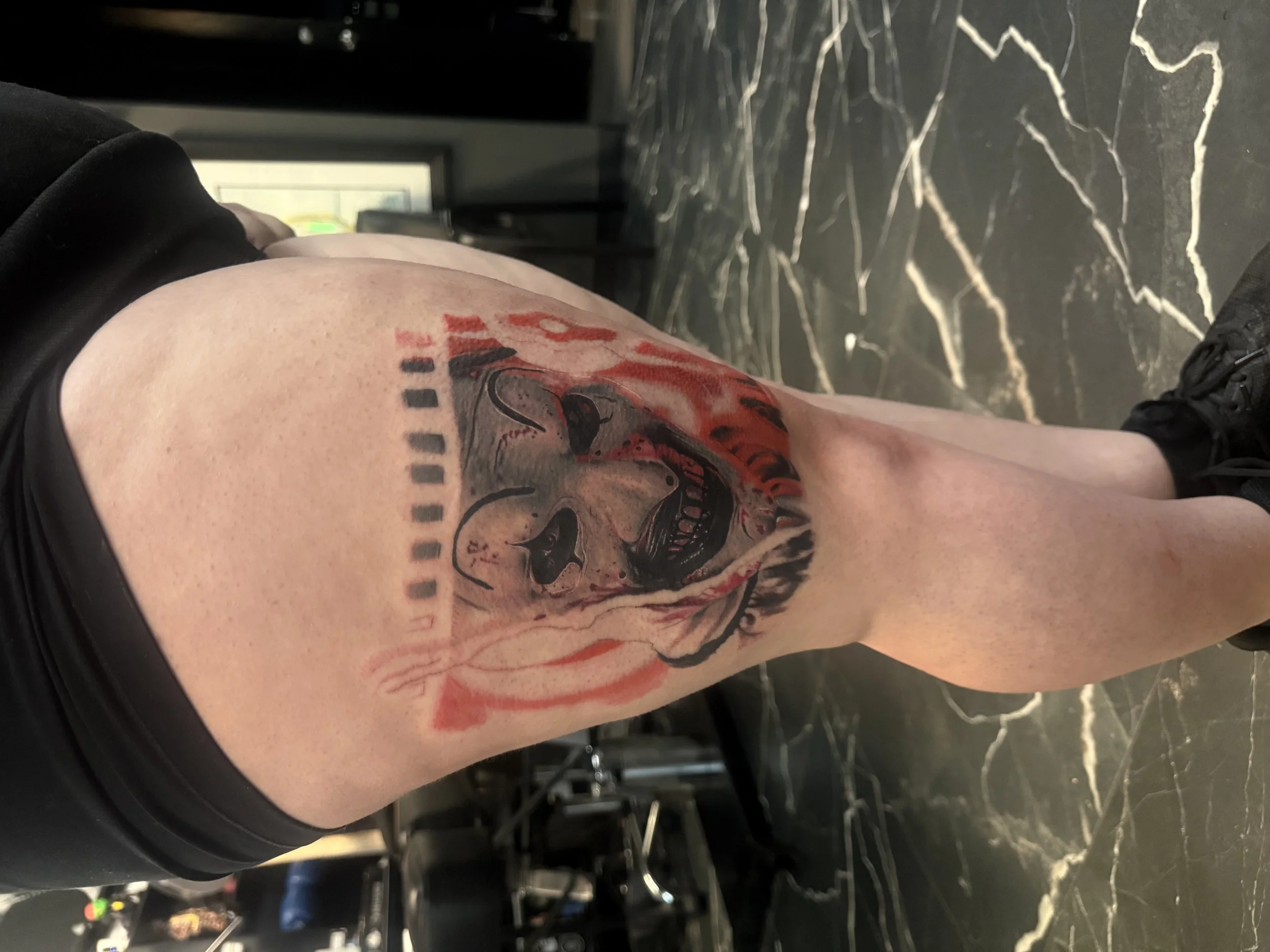 Close-up of a person's arm with a colorful tattoo of a skeleton skull and red flames, resting on a black marble surface.