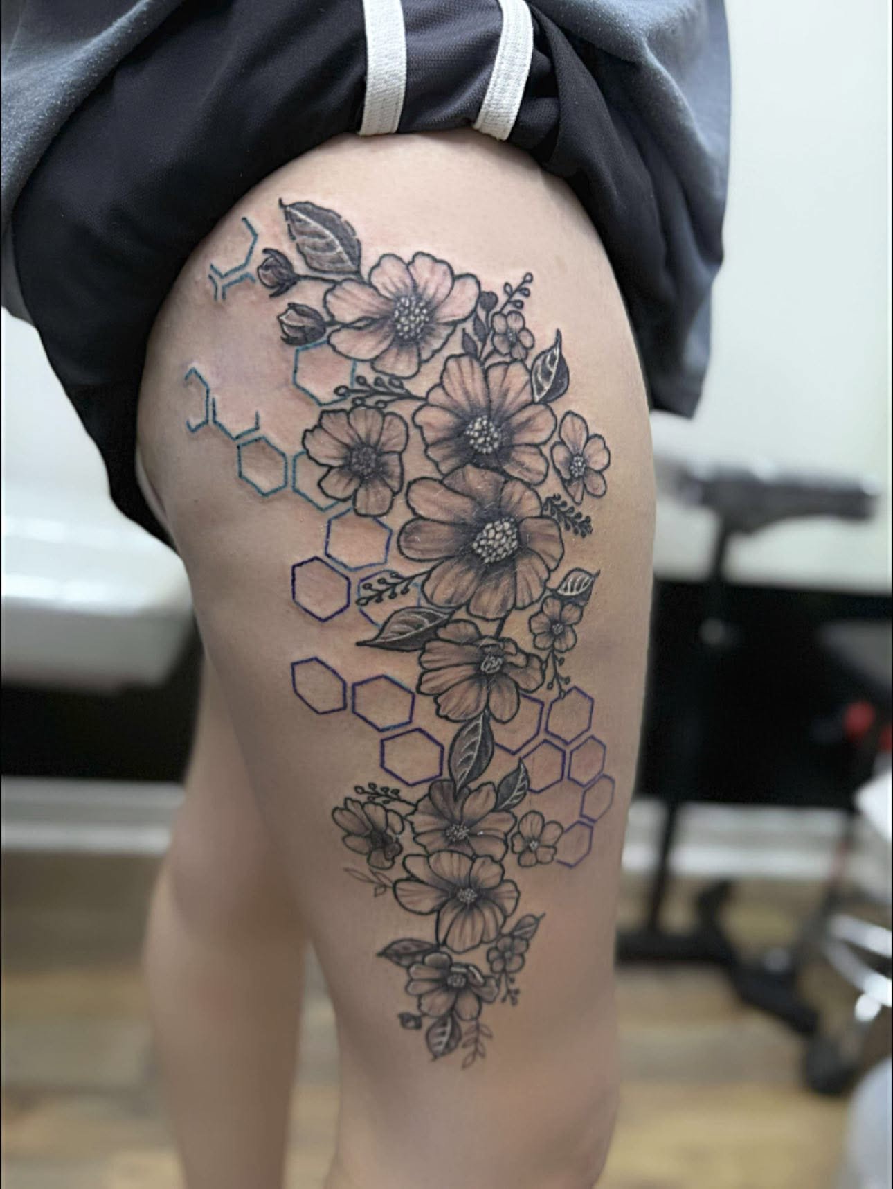 Tattoo of realistic flowers and honeycomb patterns on the person's thigh.