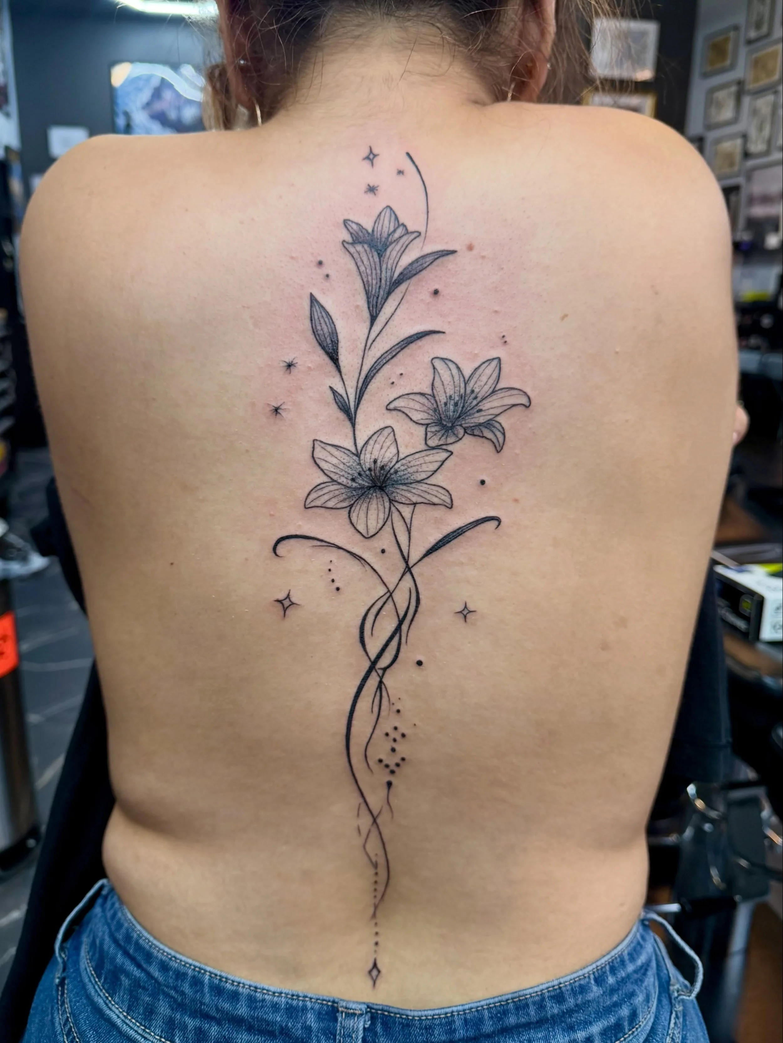 Back view of a woman with a floral tattoo extending down her spine, decorated with stars and dots.