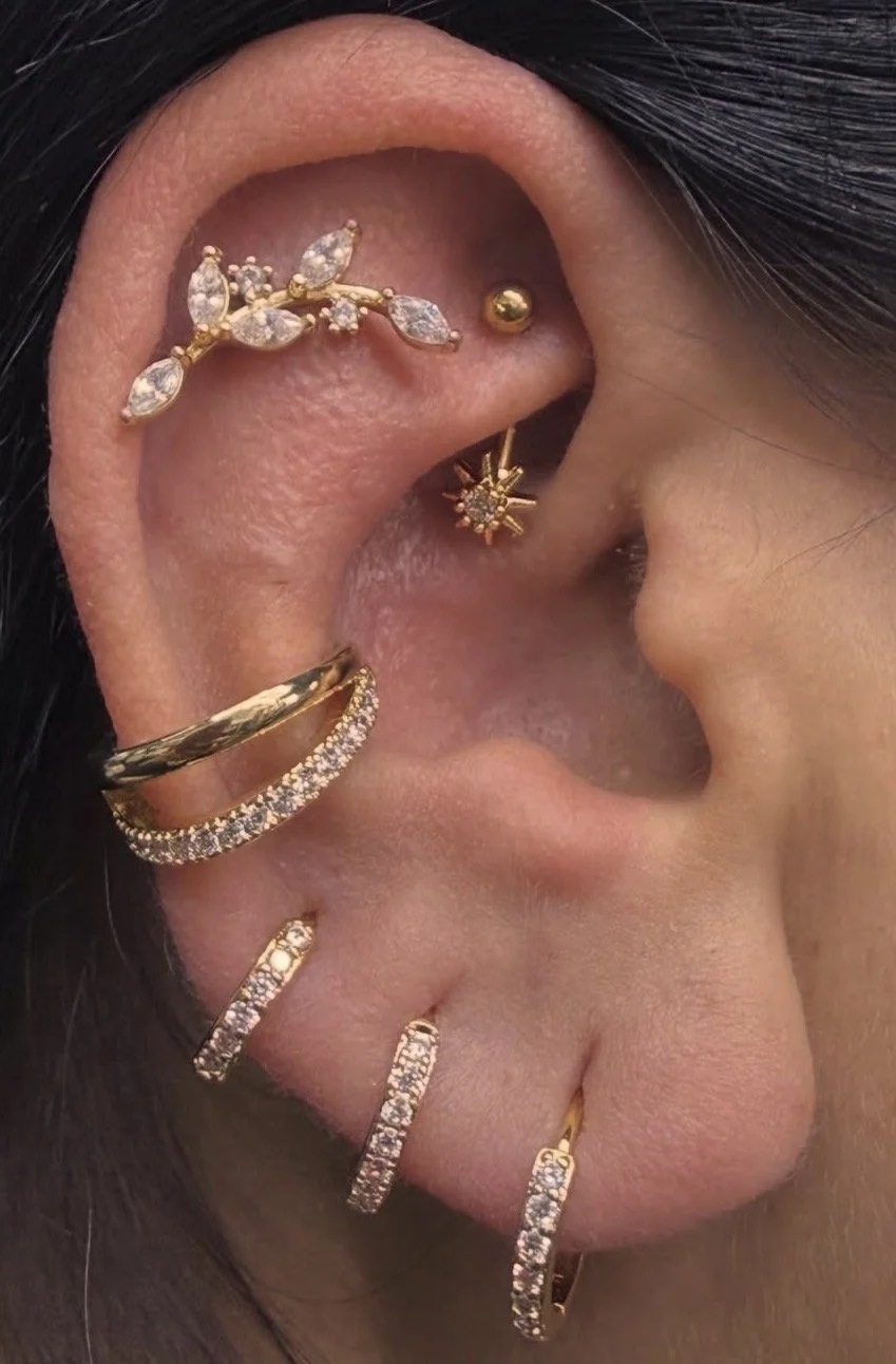 Close-up of a human ear with multiple gold and diamond earrings, including a leaf-shaped ear cuff, a star-shaped stud, and several small hoops.