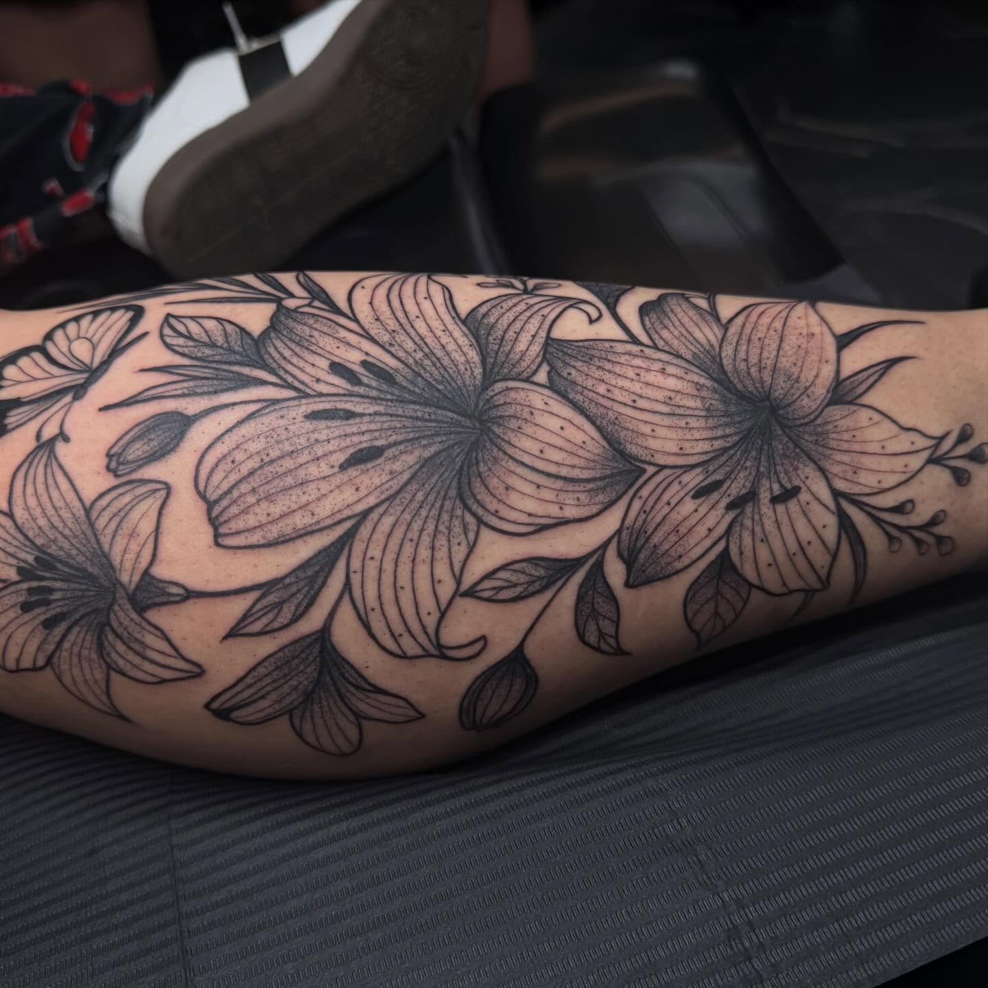 Black outline floral tattoo featuring lilies and leaves on person's arm.