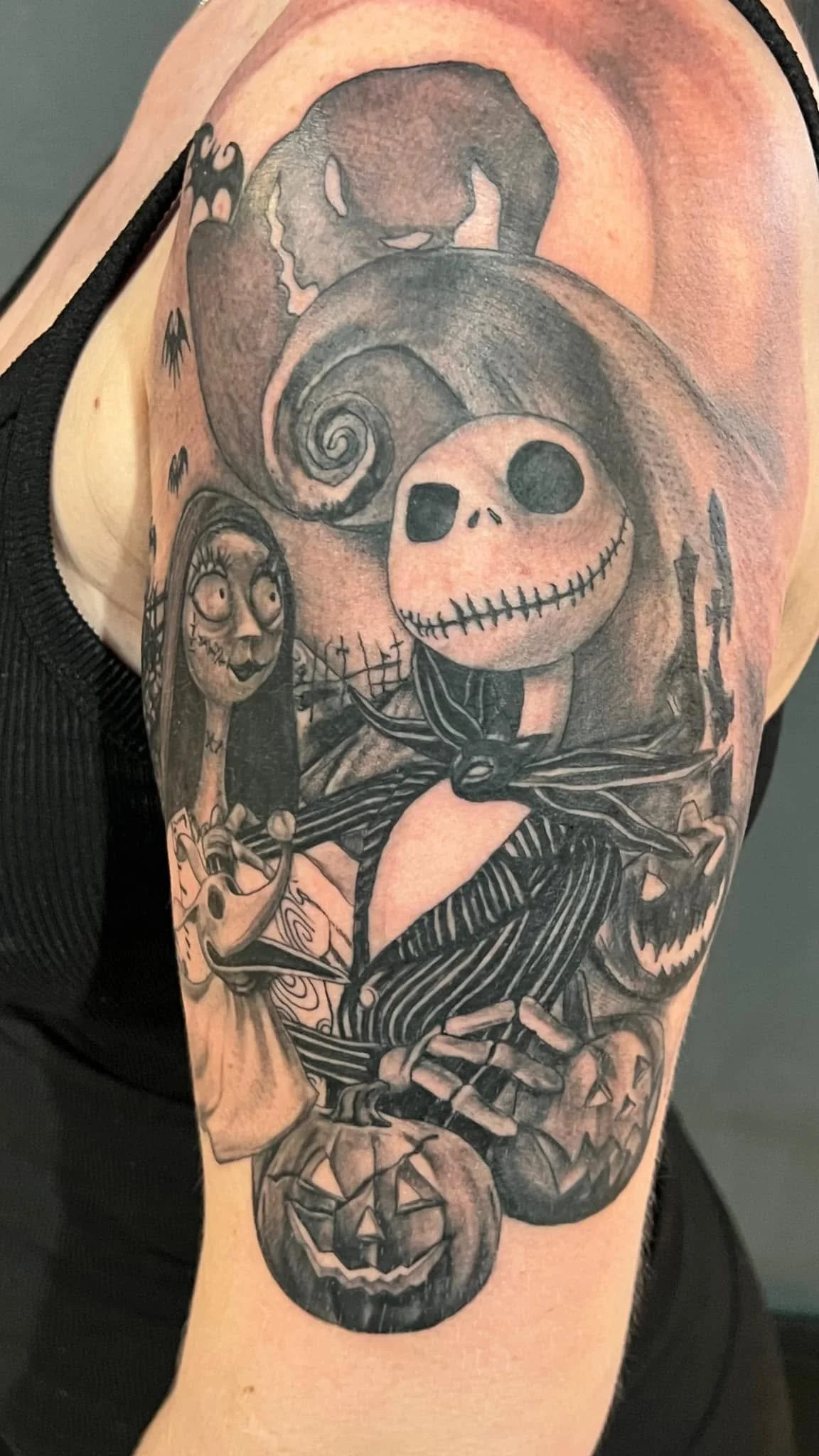 Tattoo of a skeleton with a large head and a spiral design on top. The skeleton is dressed in striped clothing and holds a broken object. The tattoo includes various dark, detailed shading.