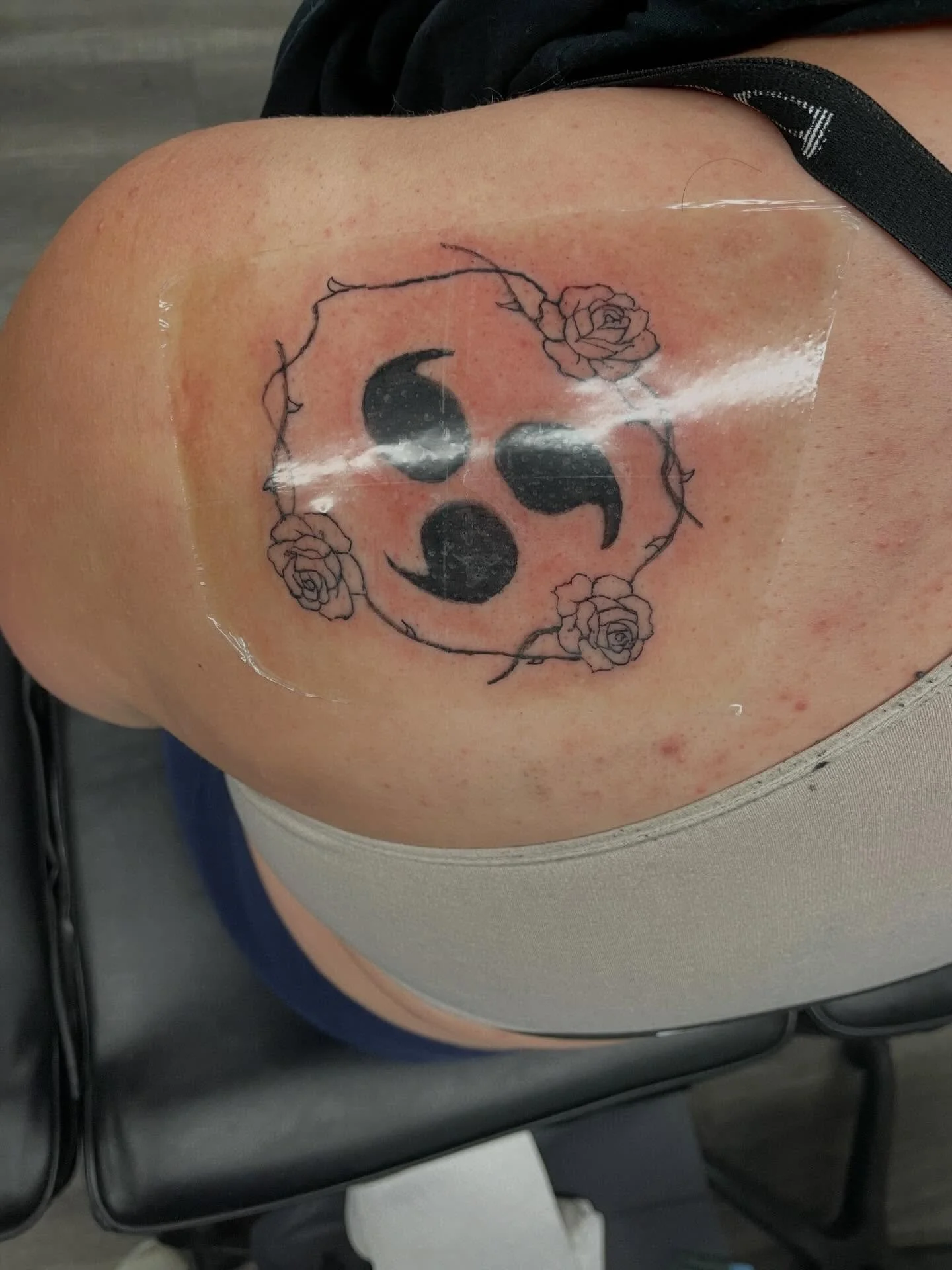 Fresh tattoo of a black and gray crescent moon with decorative roses and a circular border on a person's upper shoulder.