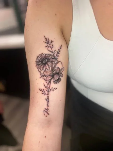 Tattoo of a flower bouquet with the words 'Mom and Dad' on the forearm of a person in a white top.