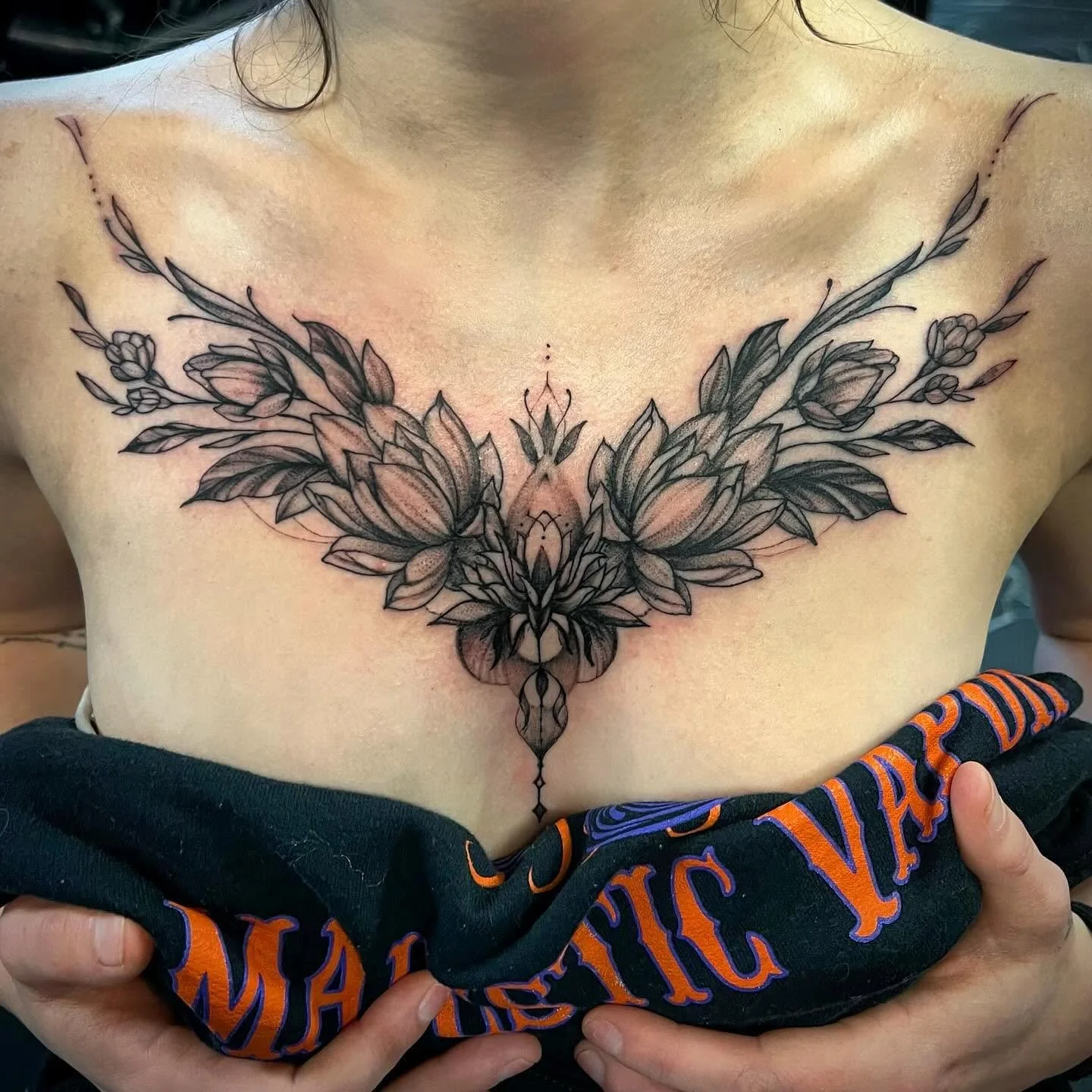 Black and gray floral-themed tattoo across the chest of a person, featuring large stylized flowers and leaves with intricate linework.
