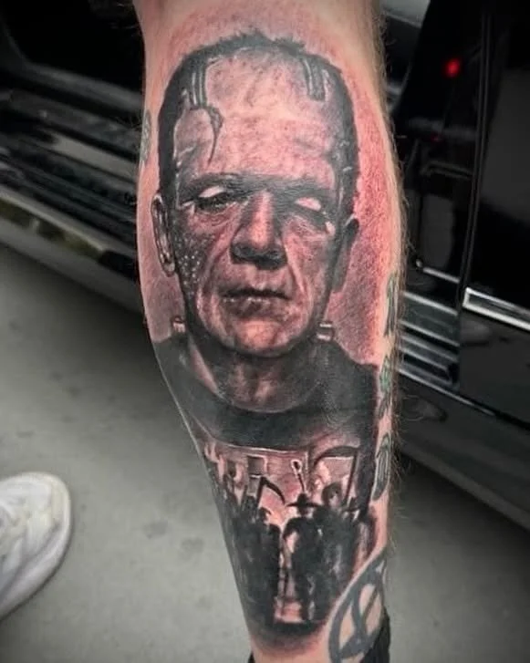 Tattoo of Frankenstein's monster with a distorted face and a figure in the background.