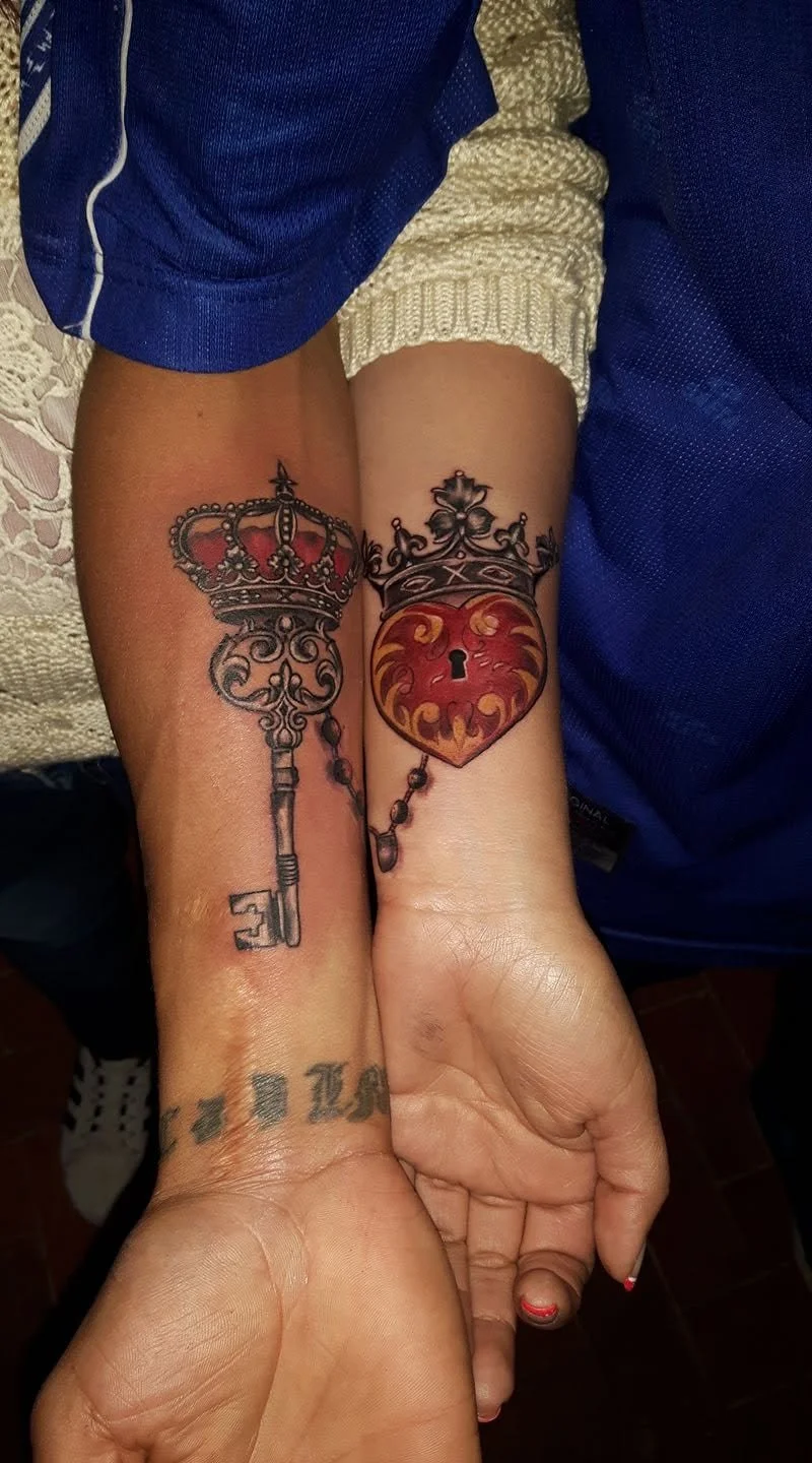 Two wrists with matching tattoos of a crown and key, and a crown and heart with a lock.