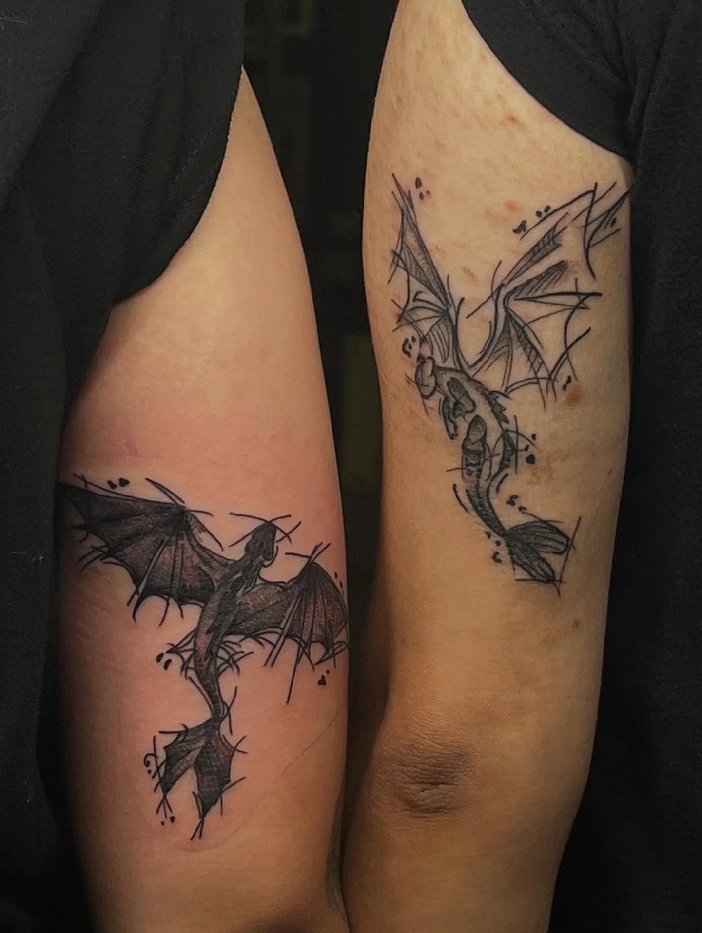 Close-up of two arms with black dragon tattoos.