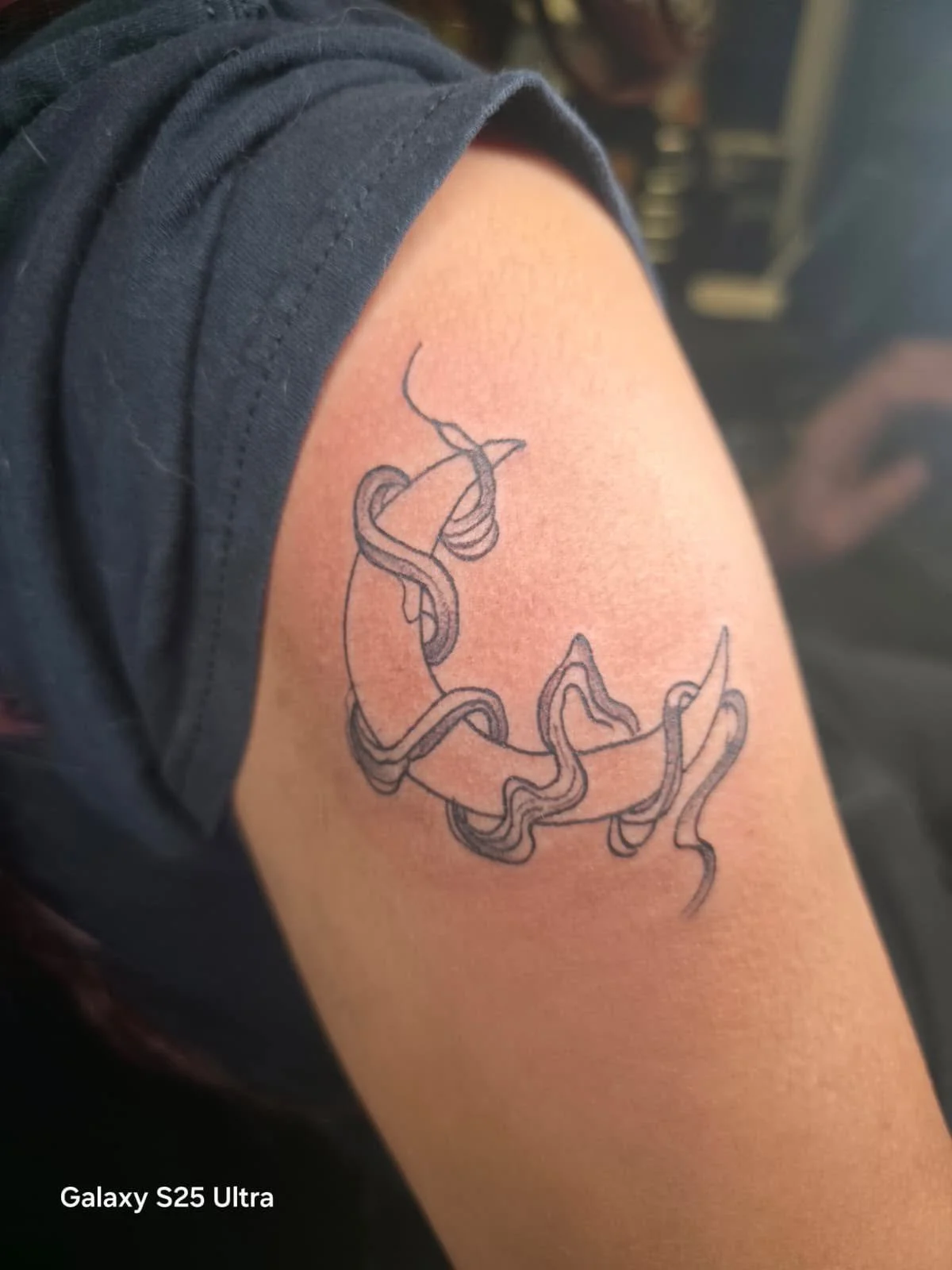 A tattoo of intertwined snake-like lines on a person's upper arm.