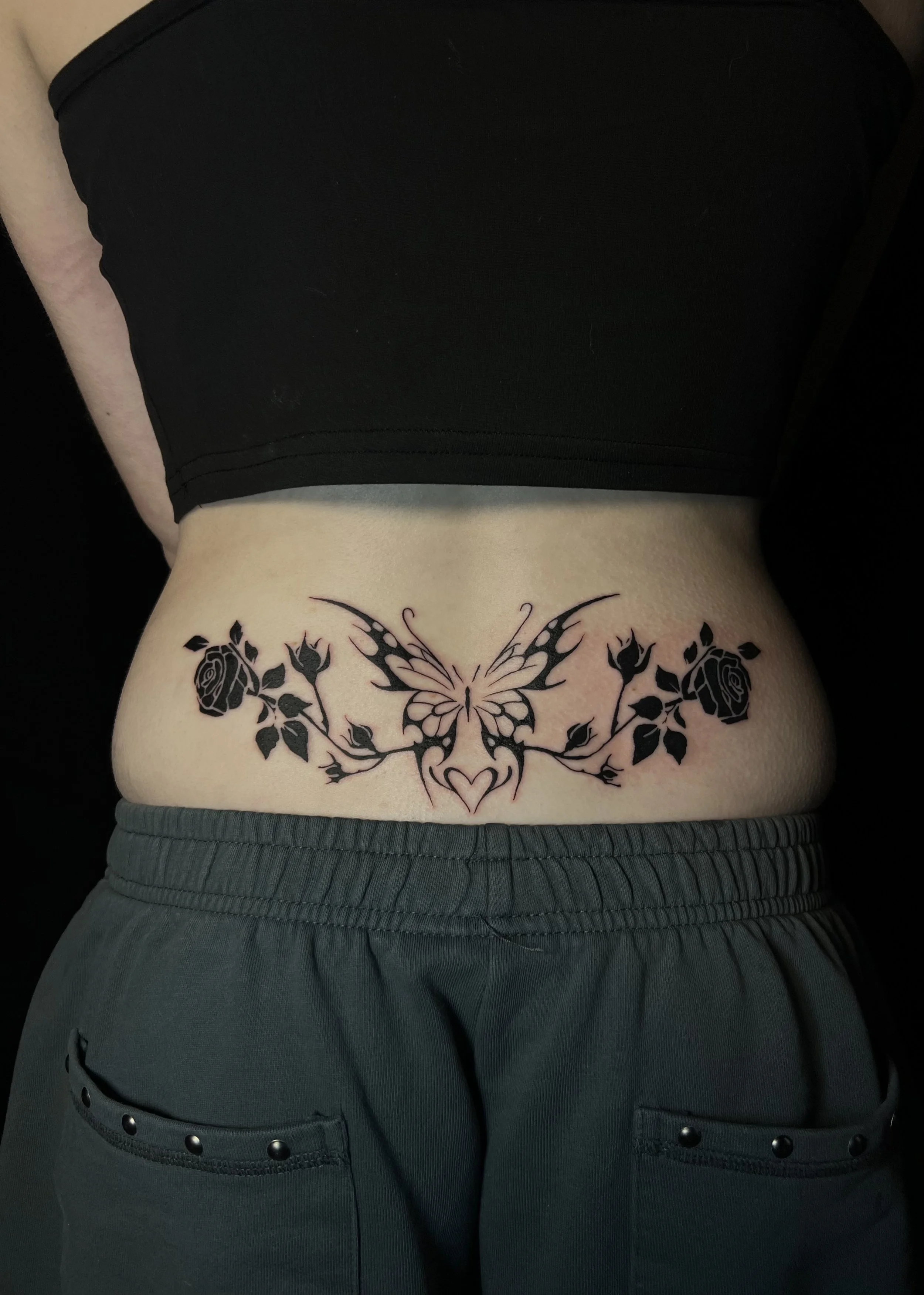 Tattoo of a butterfly with roses on lower back, worn with dark grey sweatpants and a black top.