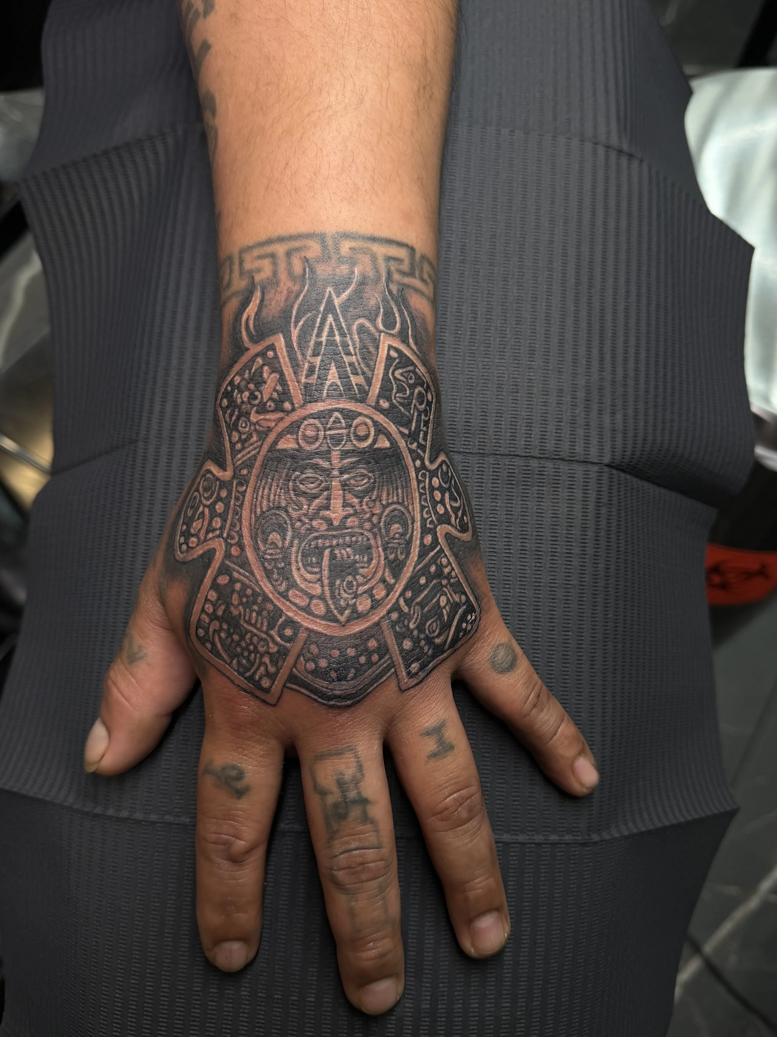 Close-up of a person's arm and hand with a detailed black tattoo of a tribal or Norse-style design, resting on their leg.