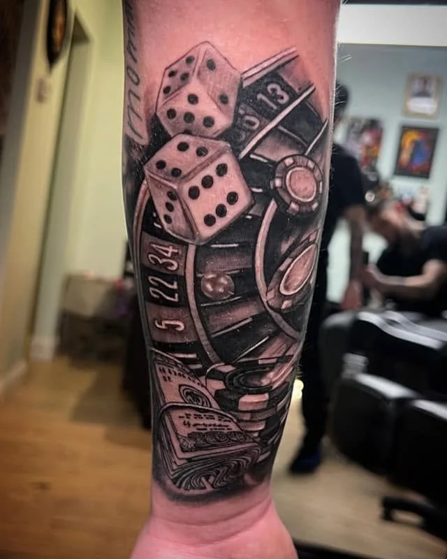Tattoo of dice, a roulette wheel, and money on a person's forearm.