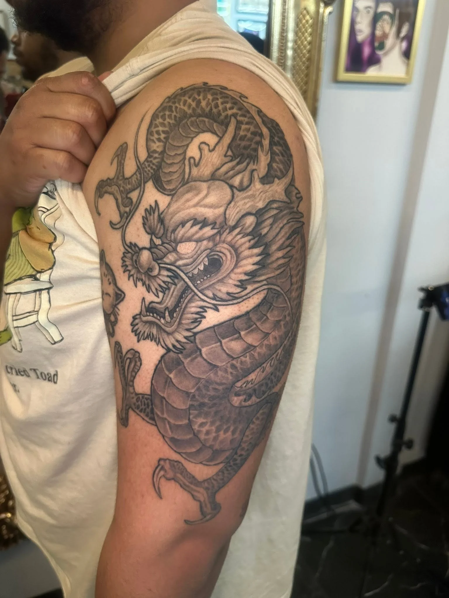 A person with a tattoo of a dragon on their upper arm and shoulder, with the dragon's head facing downward and its body coiled.