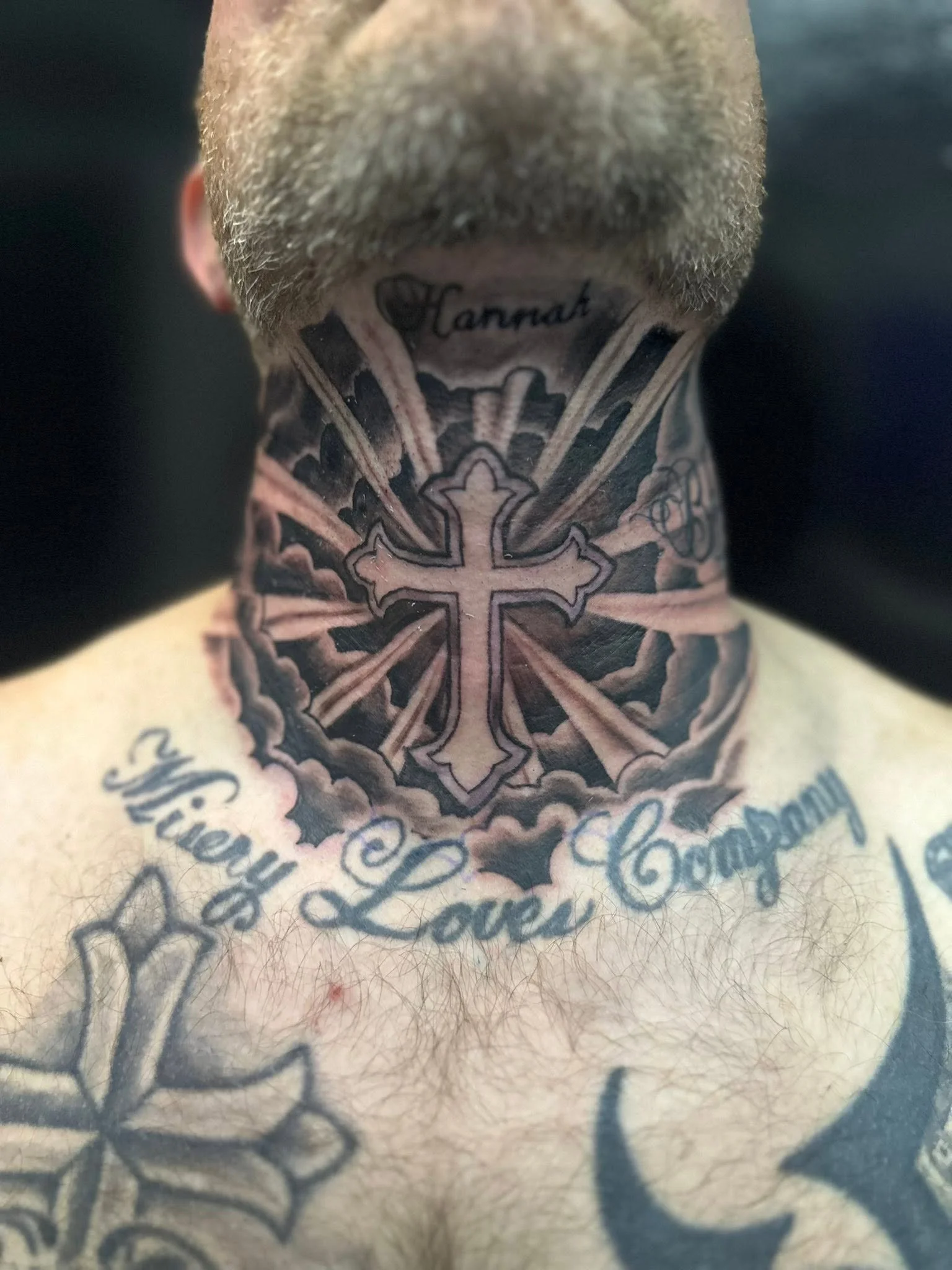 Close-up of a person's neck with tattoos, including a cross and the word 'Hannah' visible, along with some script lettering.
