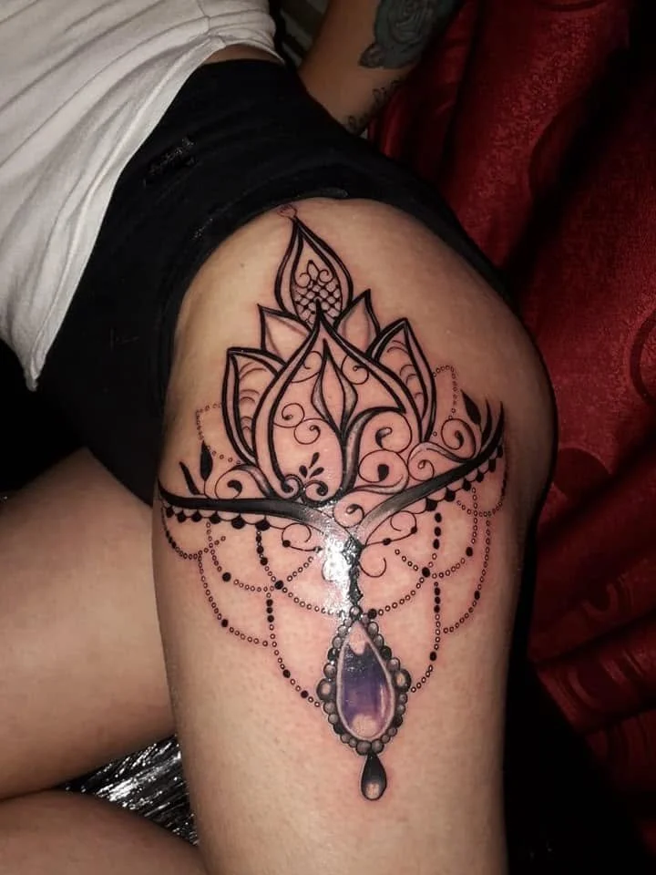A detailed black ink tattoo of a lotus flower with decorative dots and patterns on a person's upper thigh and hip area.