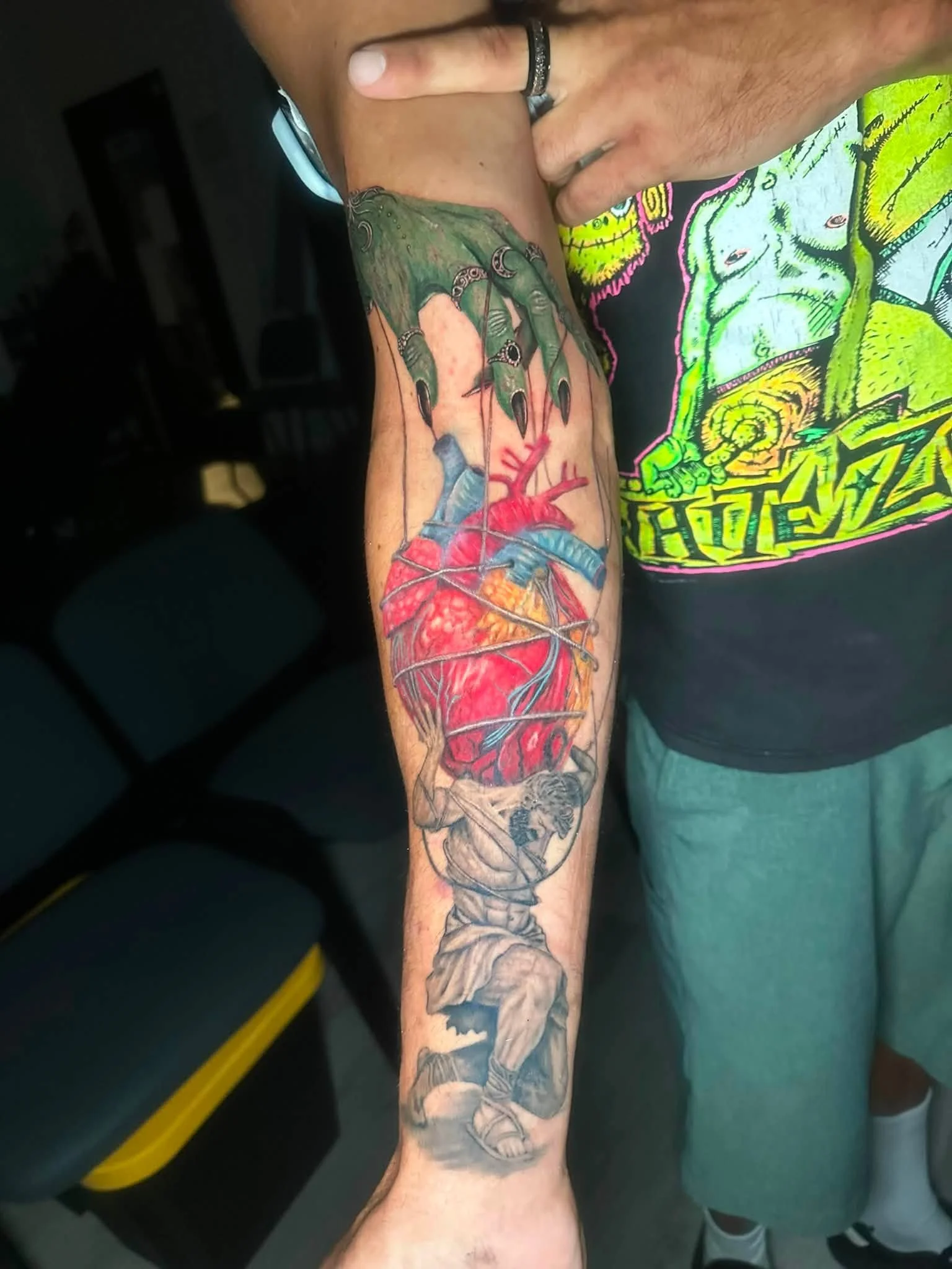 Colorful tattoo sleeve on a person's arm depicting a hand holding a heart with barbed wire, along with various other detailed designs.