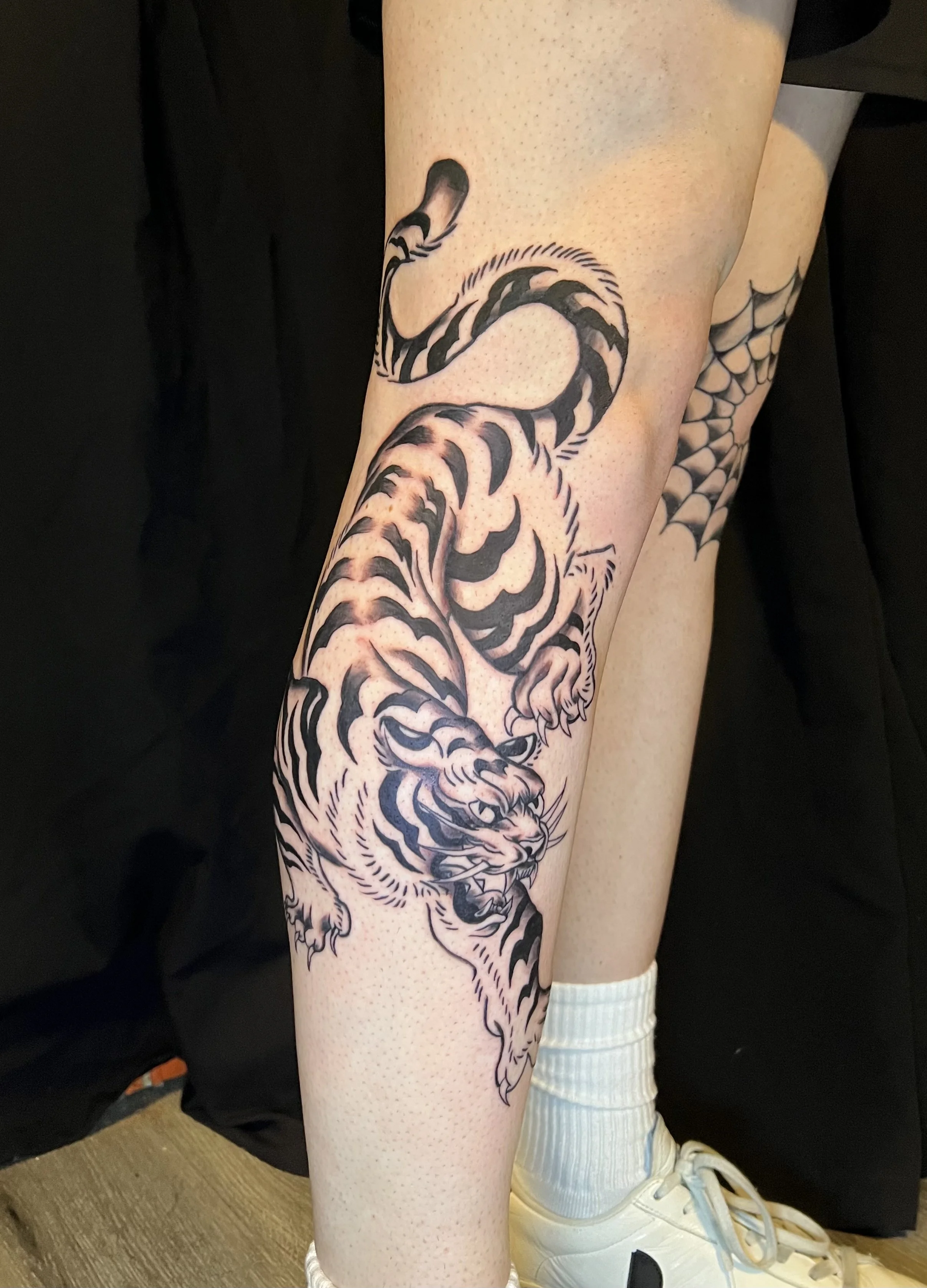 Tattoo of a tiger on a person's leg, featuring bold black outlines and detailed shading.