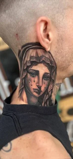 Tattoo of a woman's face with tears, on a person's neck.
