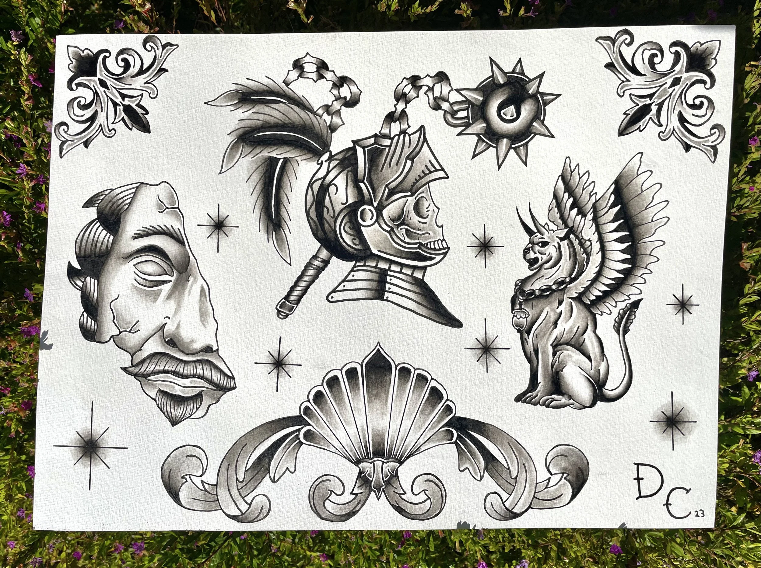 Black and white tattoo-style illustration on textured paper featuring various symbolic elements including a skull with an Egyptian headdress, a lion with a chain collar, a unicorn, a star, a spiked circular object, floral motifs, seashells, and other