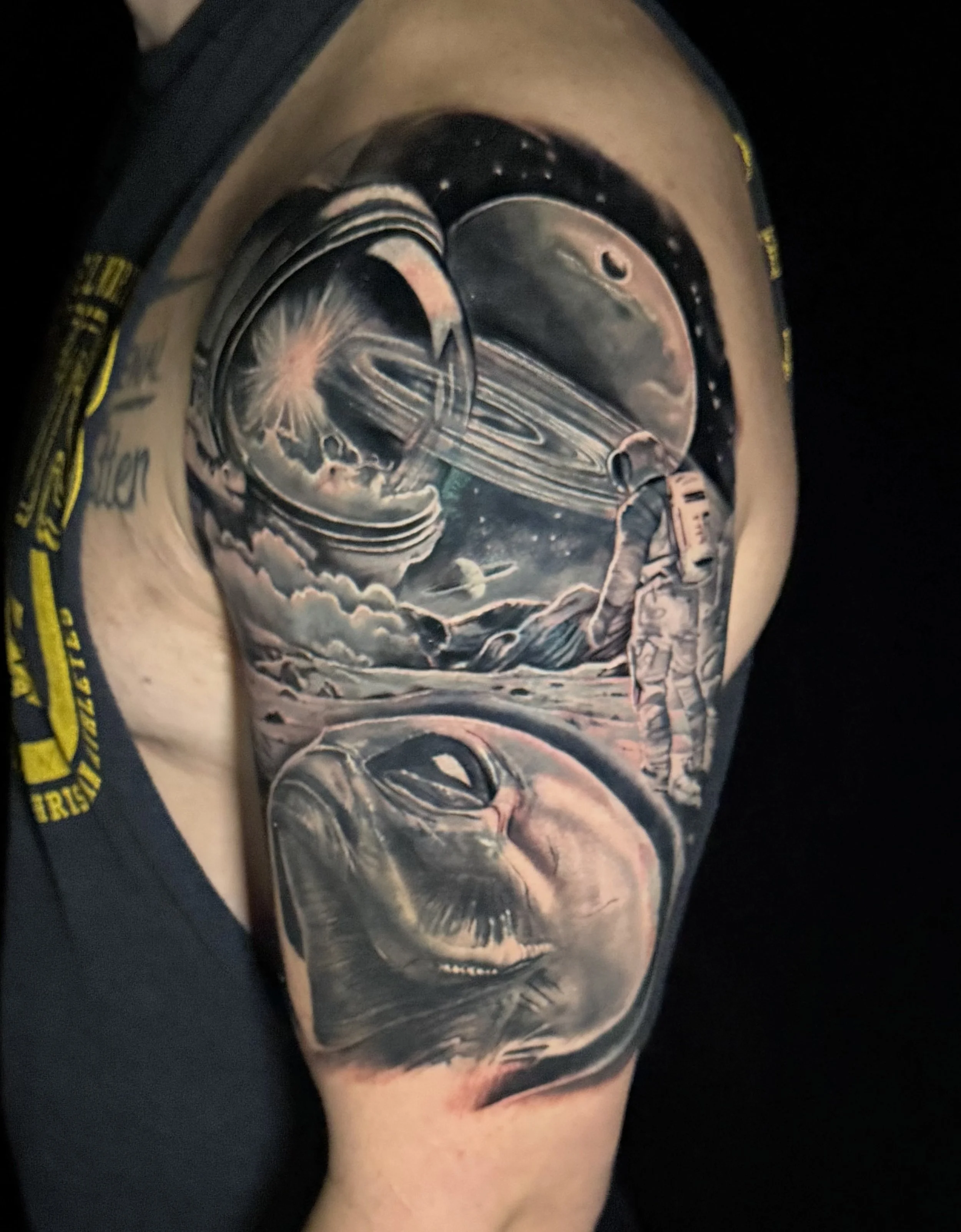 A tattoo of a space scene featuring a planet with rings, an astronaut floating, and stars.