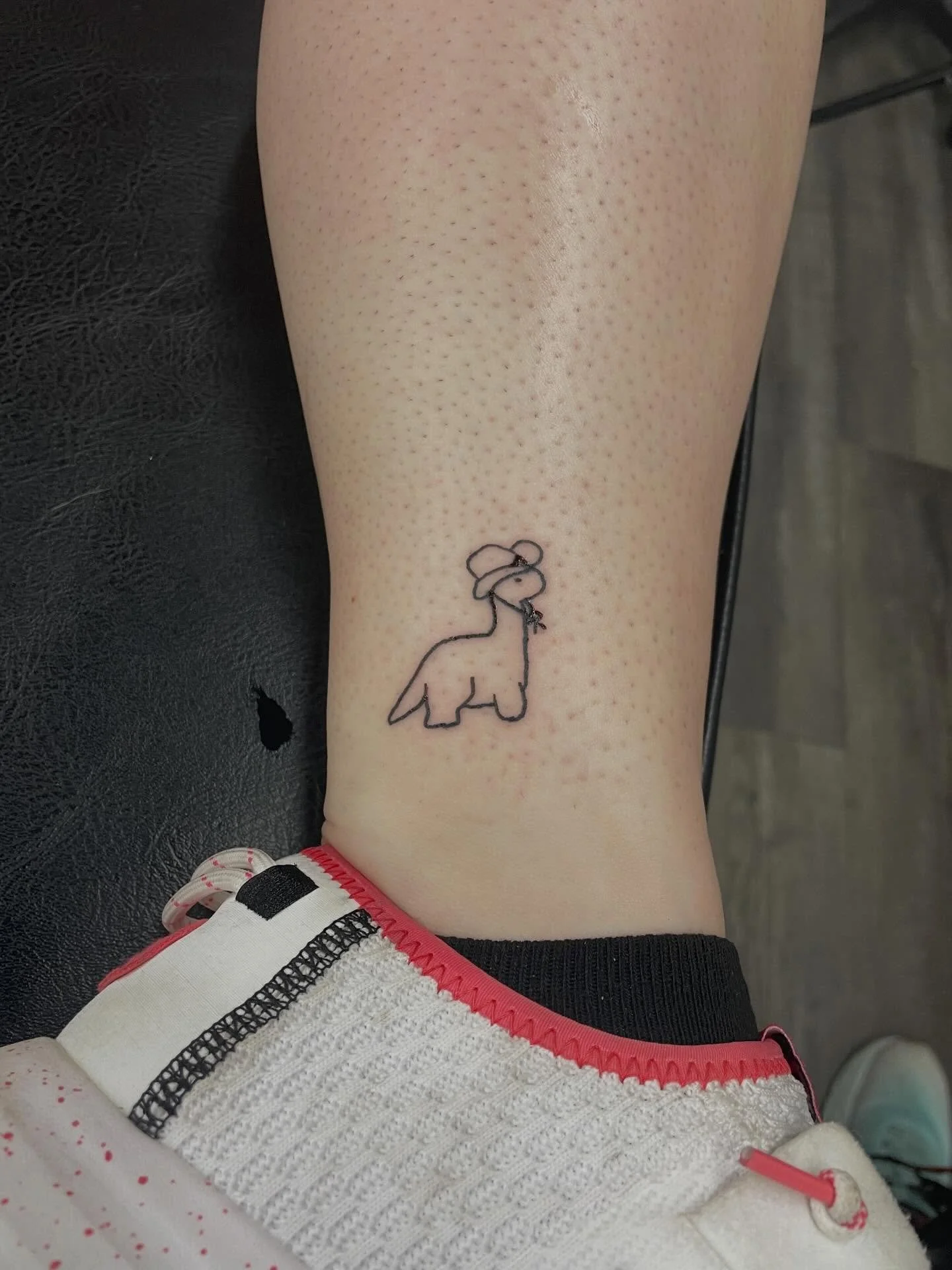 A person's leg with a small tattoo of an elephant wearing a hat. The tattoo is outlined in black. There are tiny dots all over the skin.