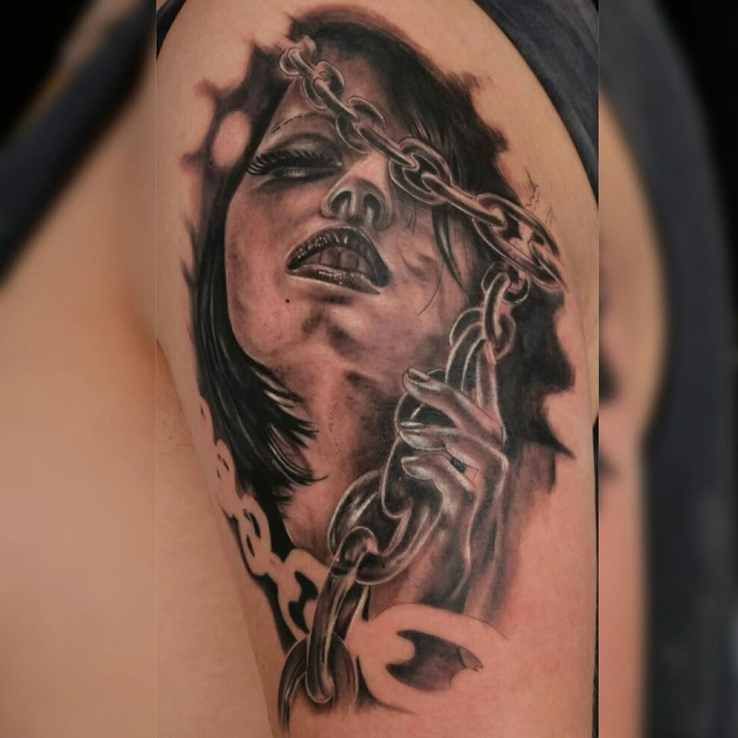 Tattoo of a woman's face with closed eyes and lips slightly parted, partly covered by a chain that wraps around her head and neck.