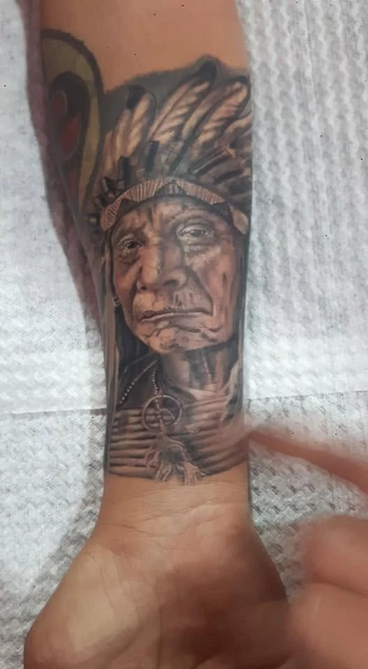 Tattoo of a Native American elder wearing a headdress on a person's forearm.