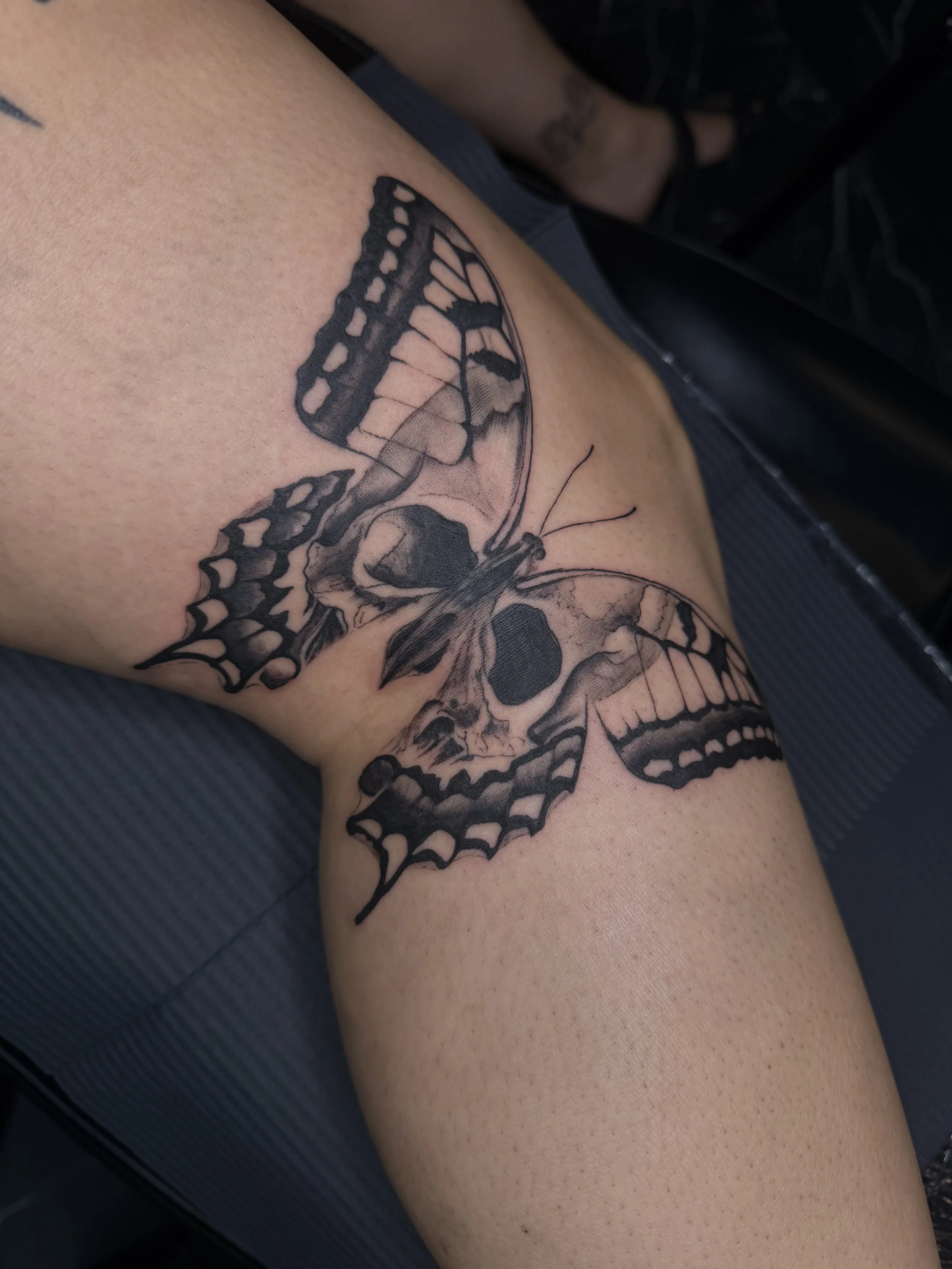 Close-up of a person's thigh with a black butterfly tattoo.