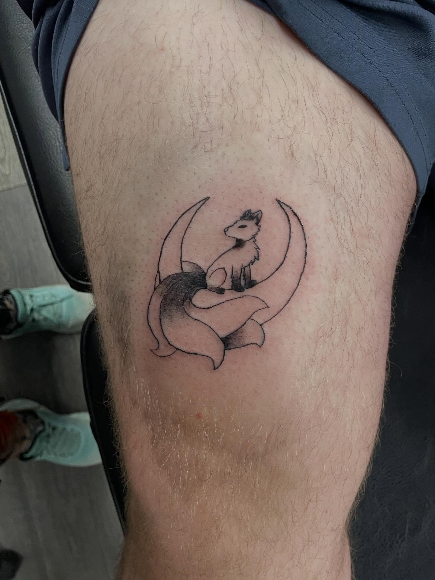 Tattoo of a fox sitting on a crescent moon on person's thigh.