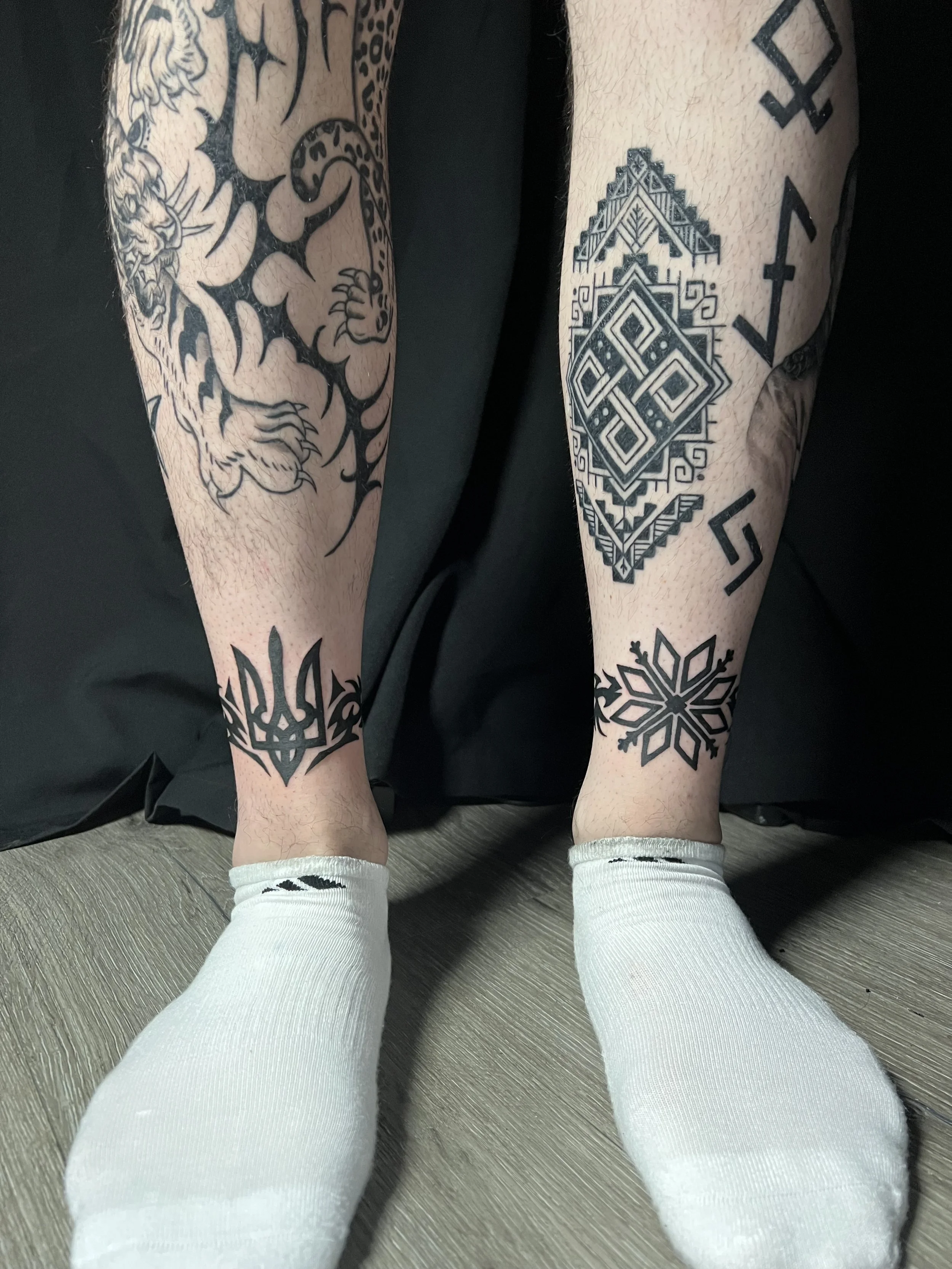 Close-up of two legs with tattoos, wearing white socks, on a beige carpeted floor.