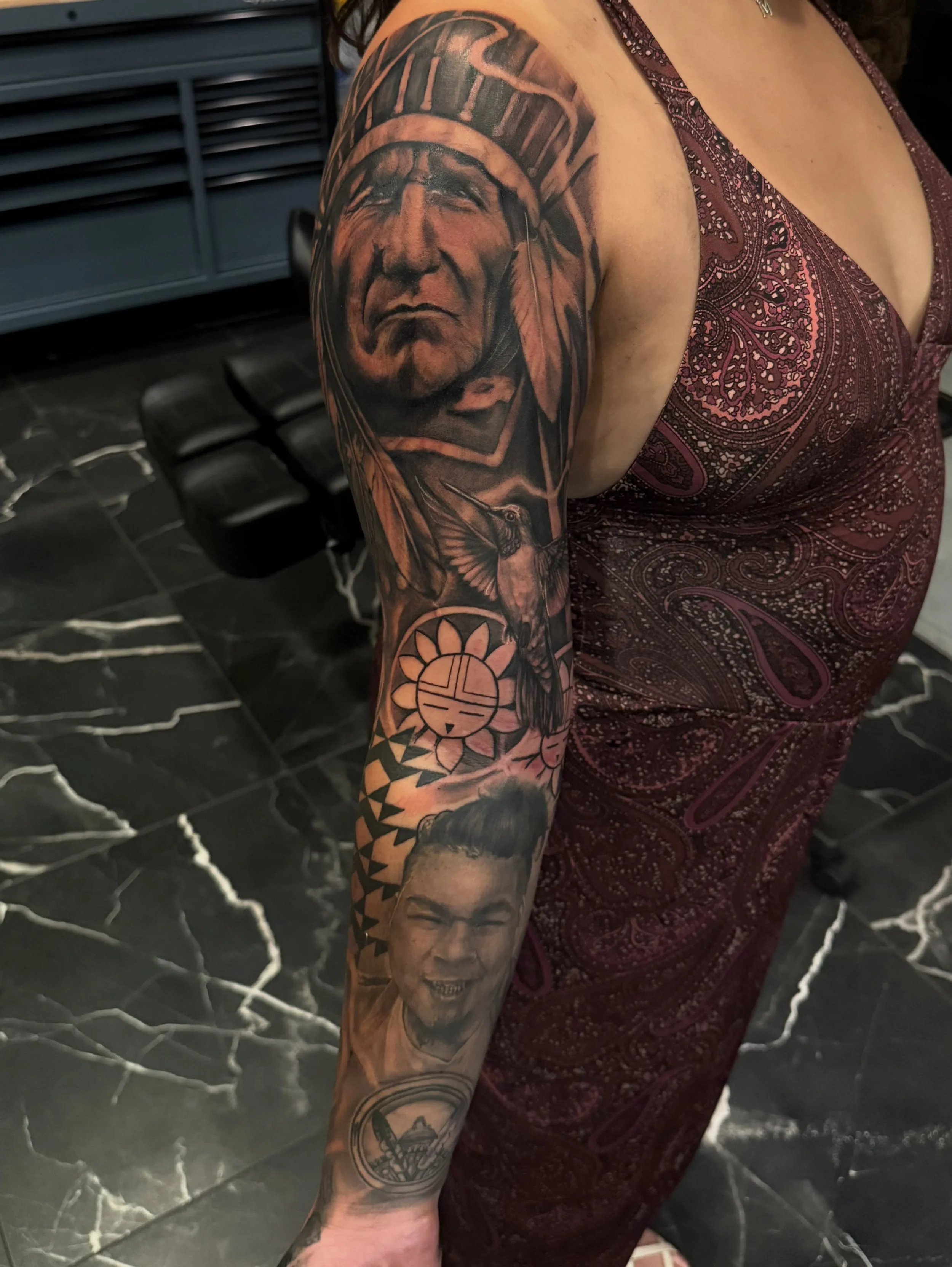 Tattoo of a Native American chief with a feathered headdress and a stern expression on the upper arm.