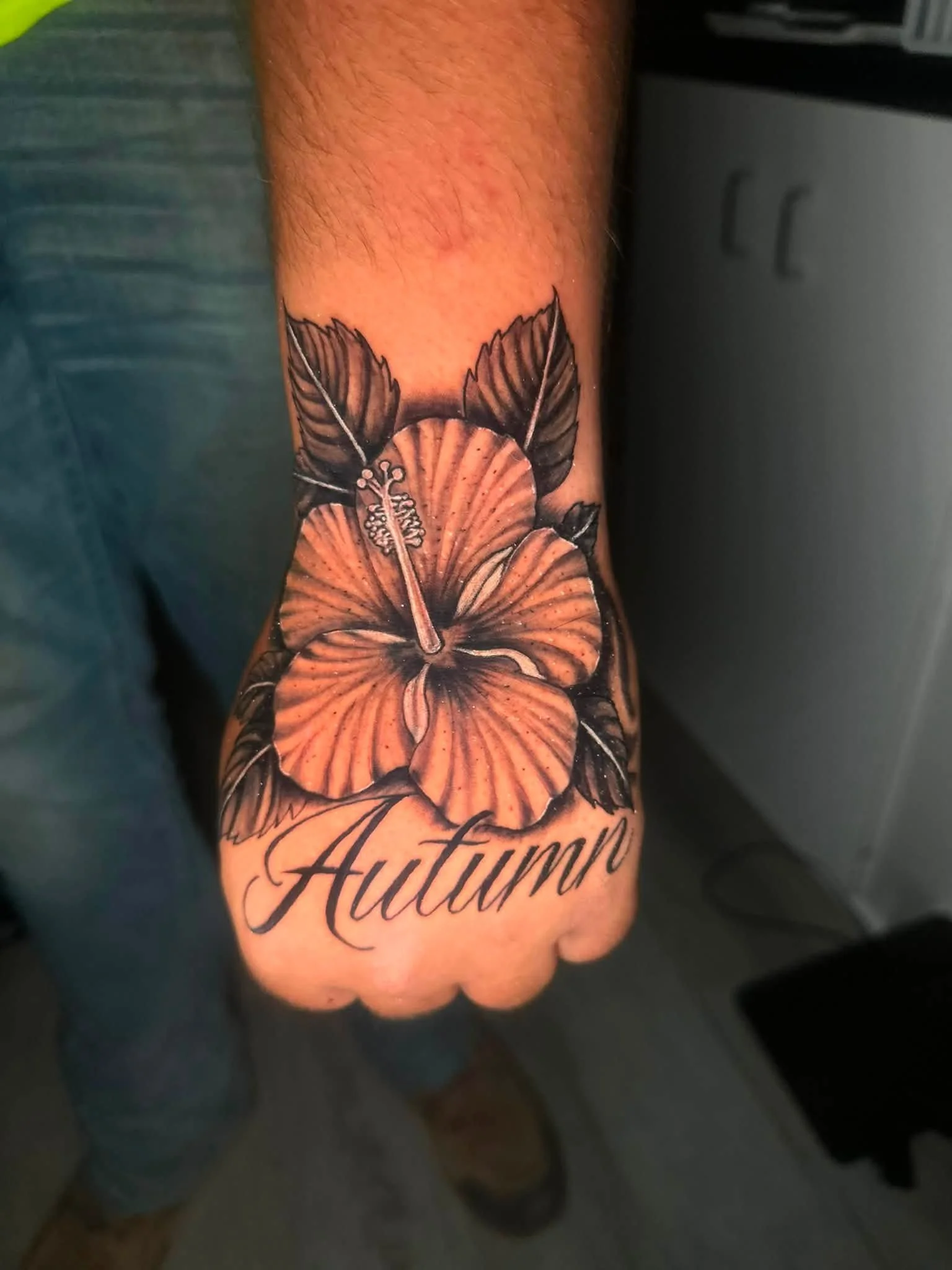 A tattoo on a person's arm of two hibiscus flowers and the word 'Autumn' in cursive.