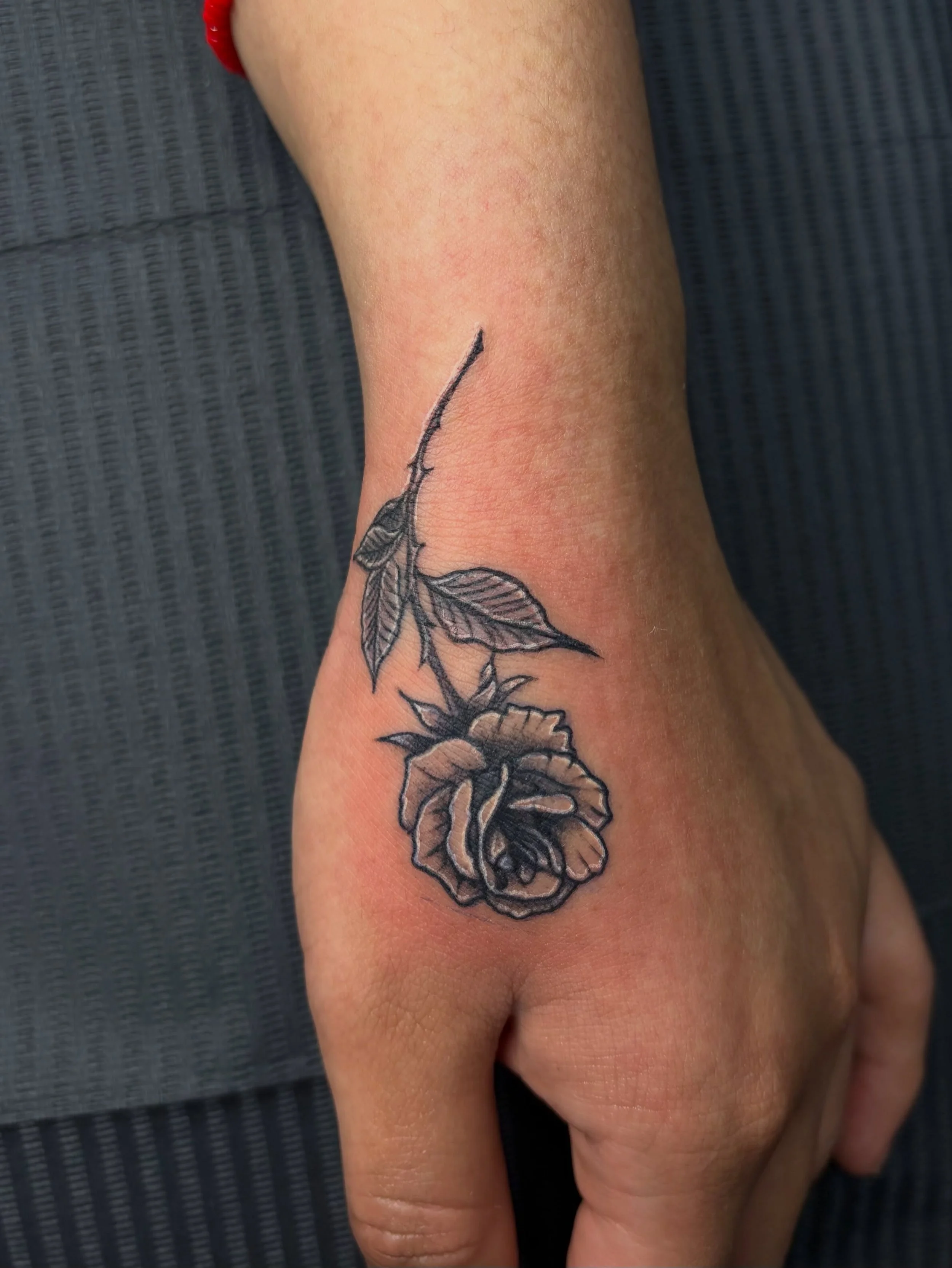 A close-up of a person's hand with a butterfly tattoo on the wrist. The tattoo features outlined black ink with some shaded areas, and the wrist appears to be slightly red or irritated.
