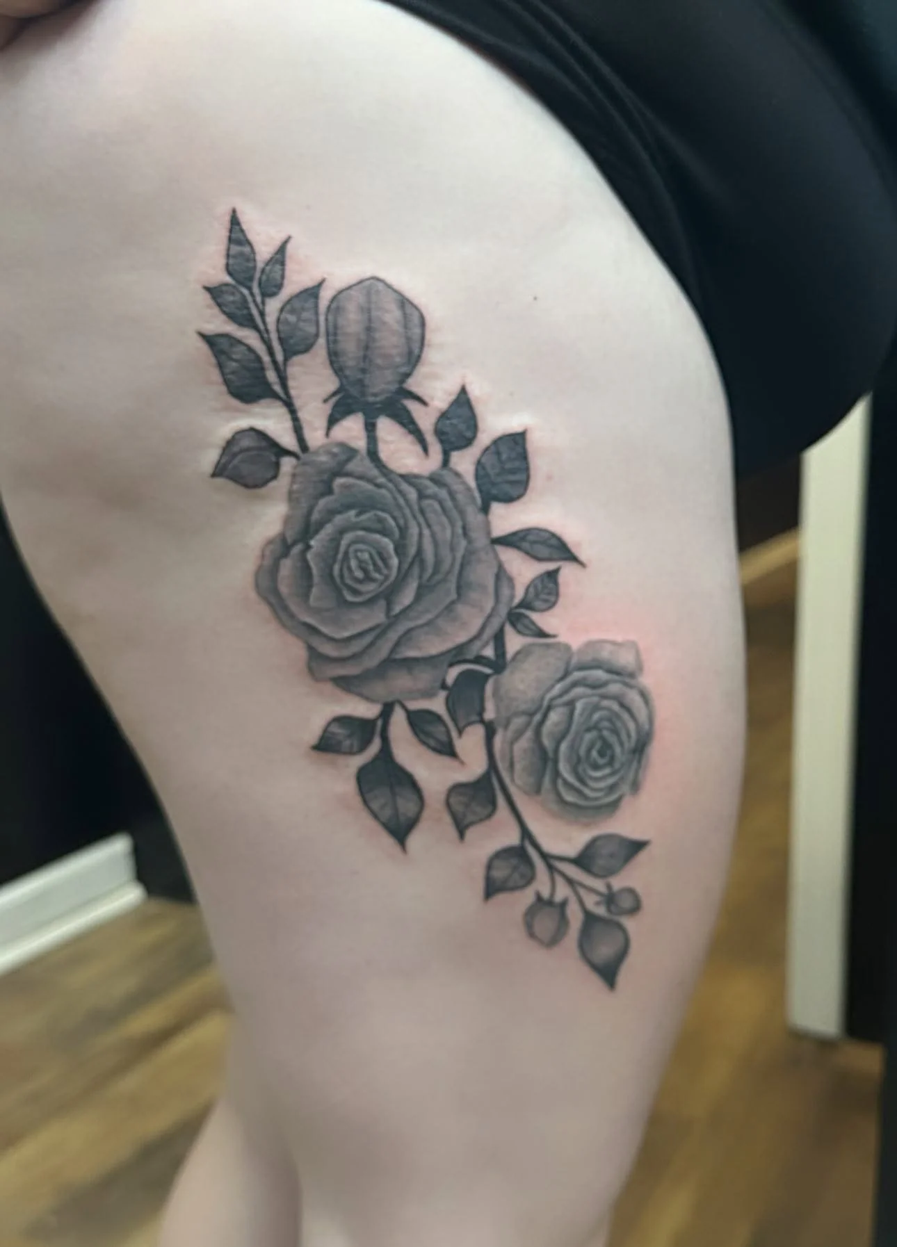 Black and gray floral tattoo of roses and leaves on person's upper arm near shoulder.