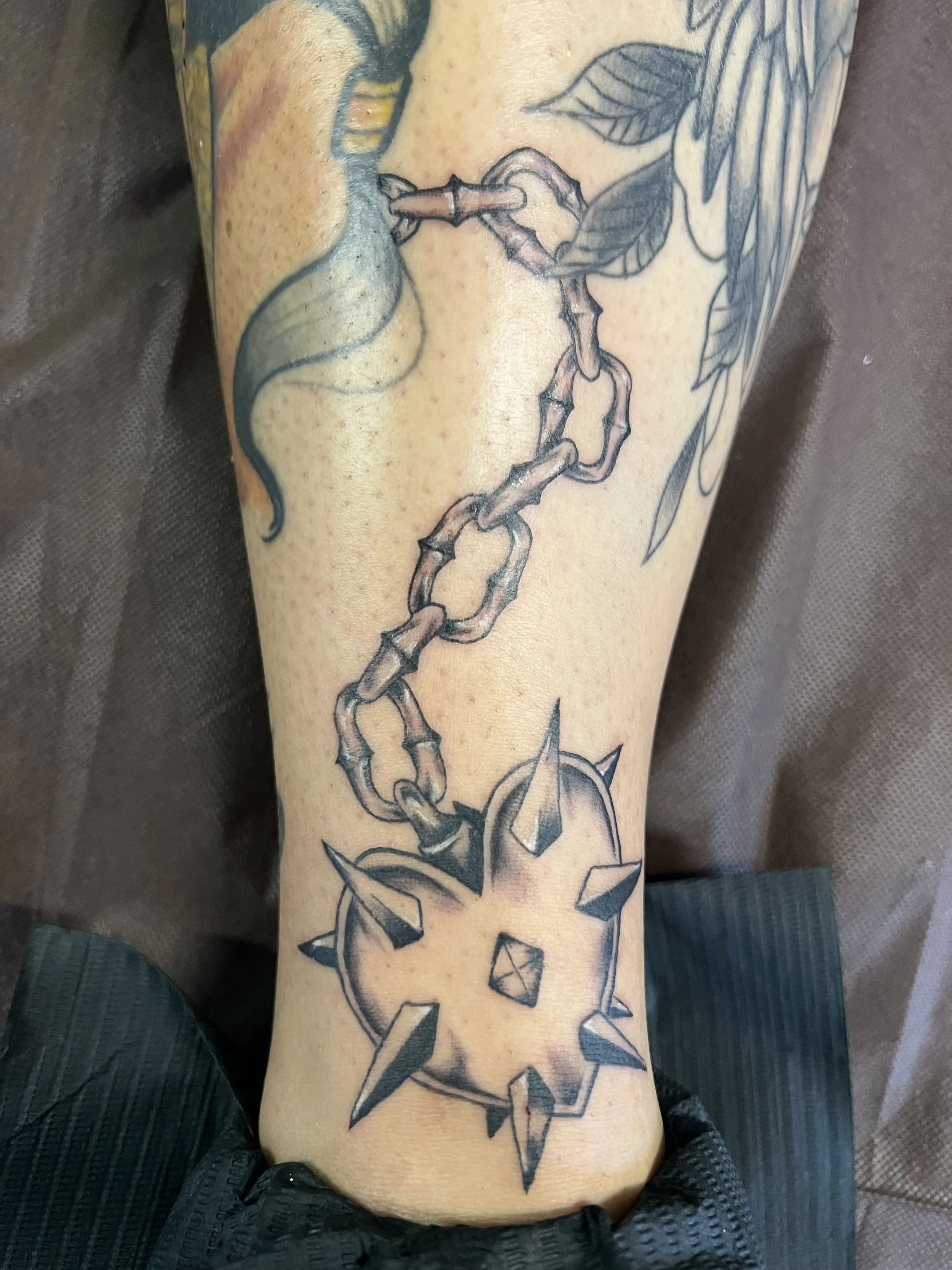 A tattoo of a snake intertwined with a chain, with leaves and geometric shapes surrounding it on a person's forearm.