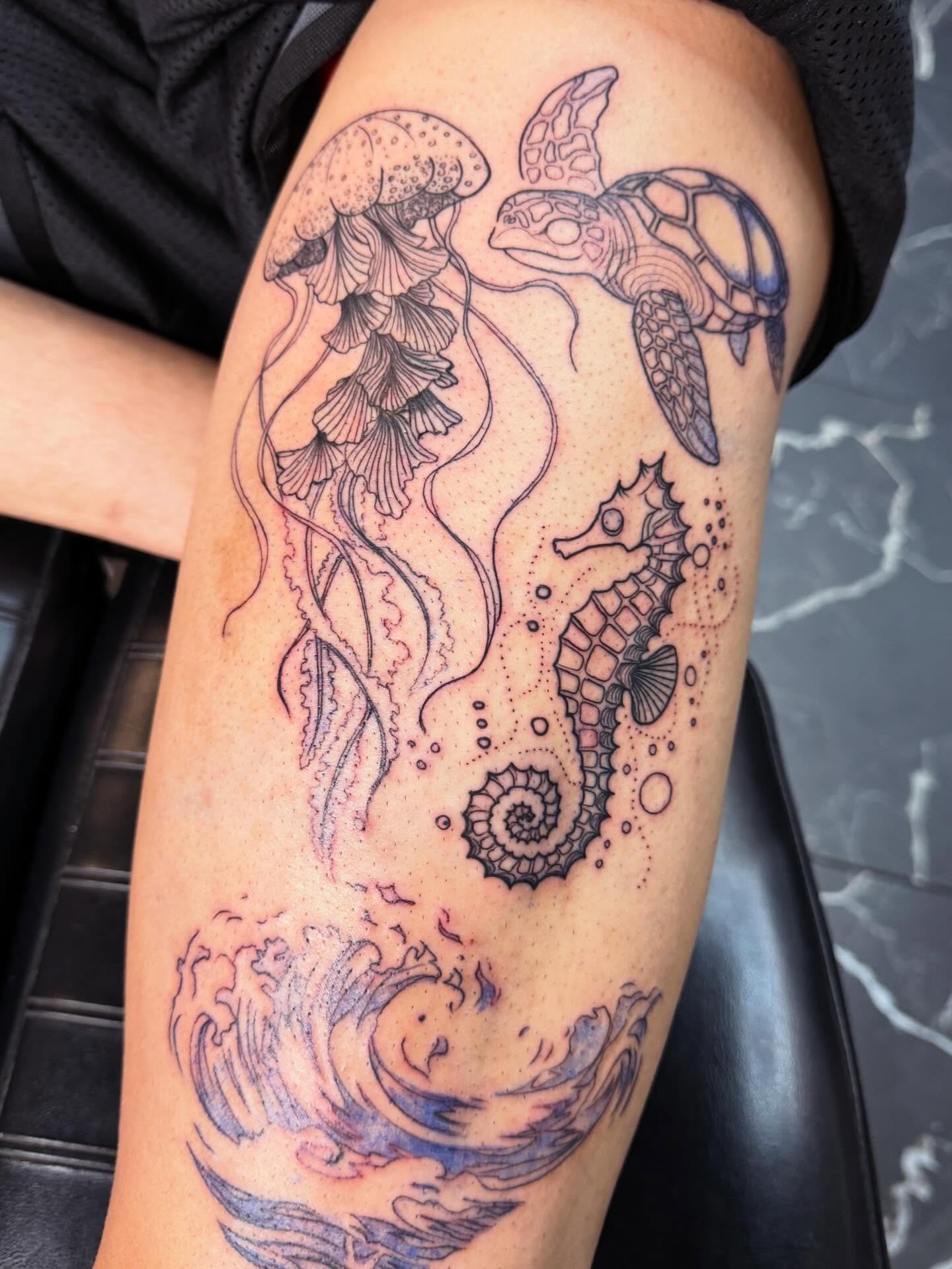 Line art tattoo of a jellyfish, seahorse, turtle, and wave on a person's arm.