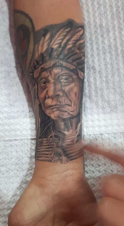 Tattoo of an elderly Native American man wearing a feathered headdress on a person's forearm.