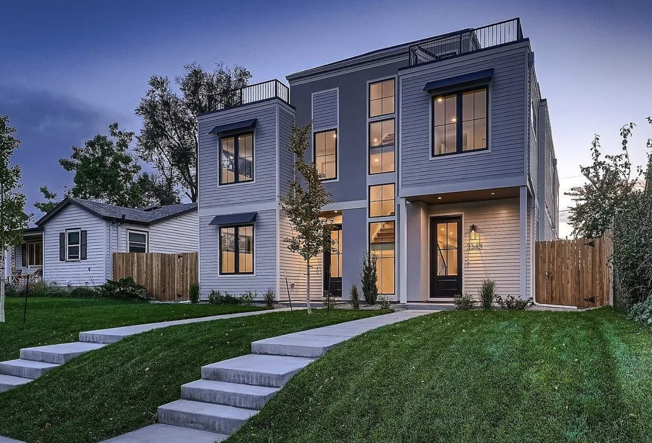 Modern multi-story house with large windows, a landscaped front yard, and a walkway with steps leading to the entrance, during twilight.