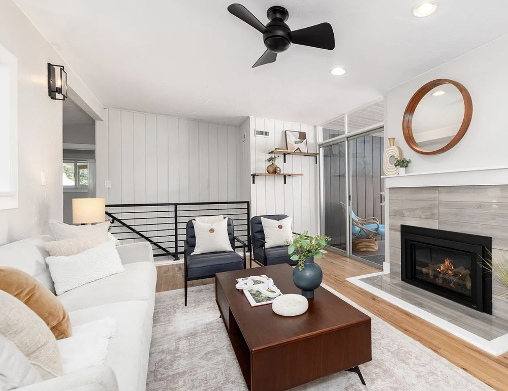 Living room with white sofa, black armchairs, wood coffee table, fireplace, ceiling fan, and sliding door to outdoor patio.