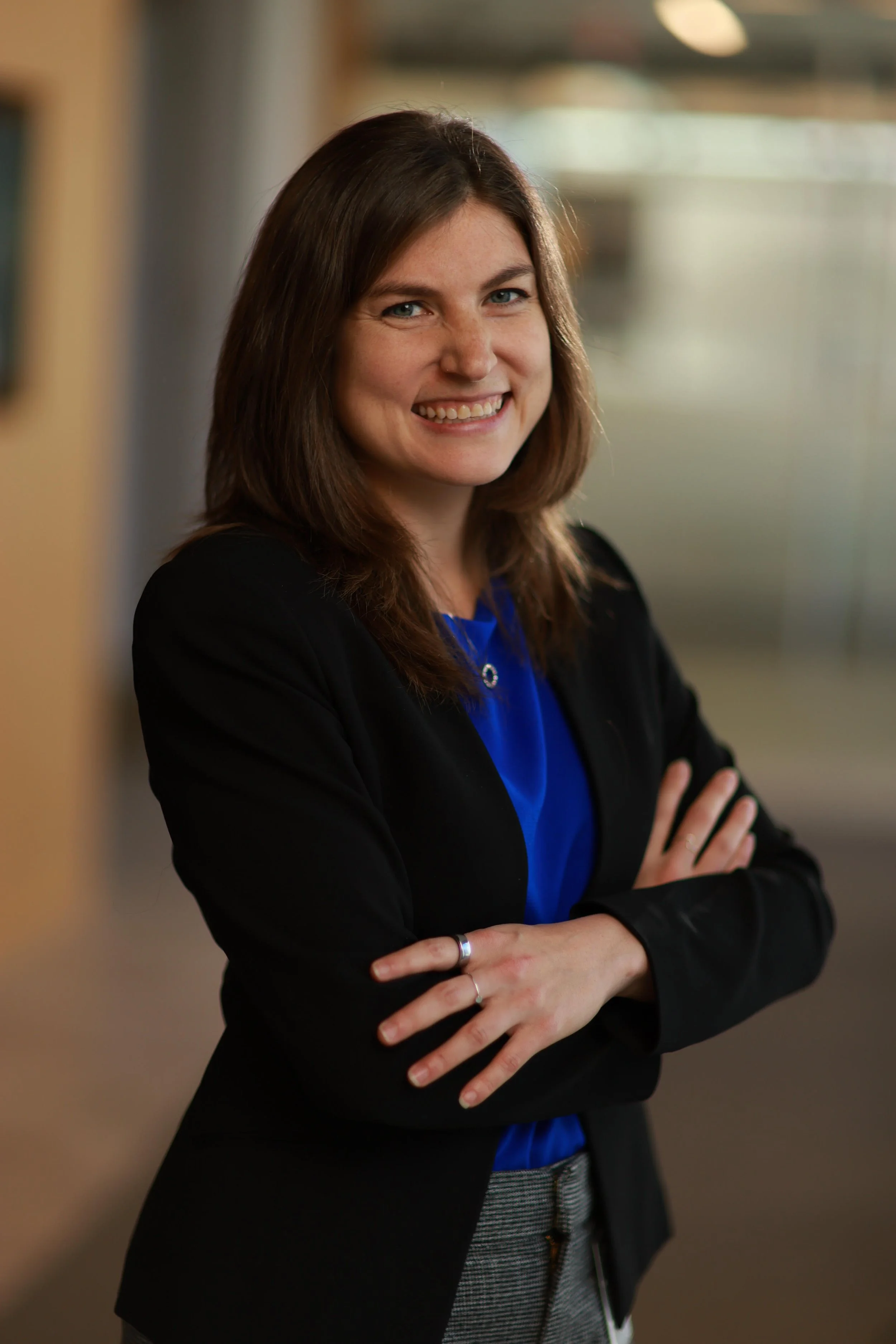 Owner and founder Shira Stoll has brown hair and is smiling, wearing a black blazer and blue top, standing with arms crossed in a professional setting.