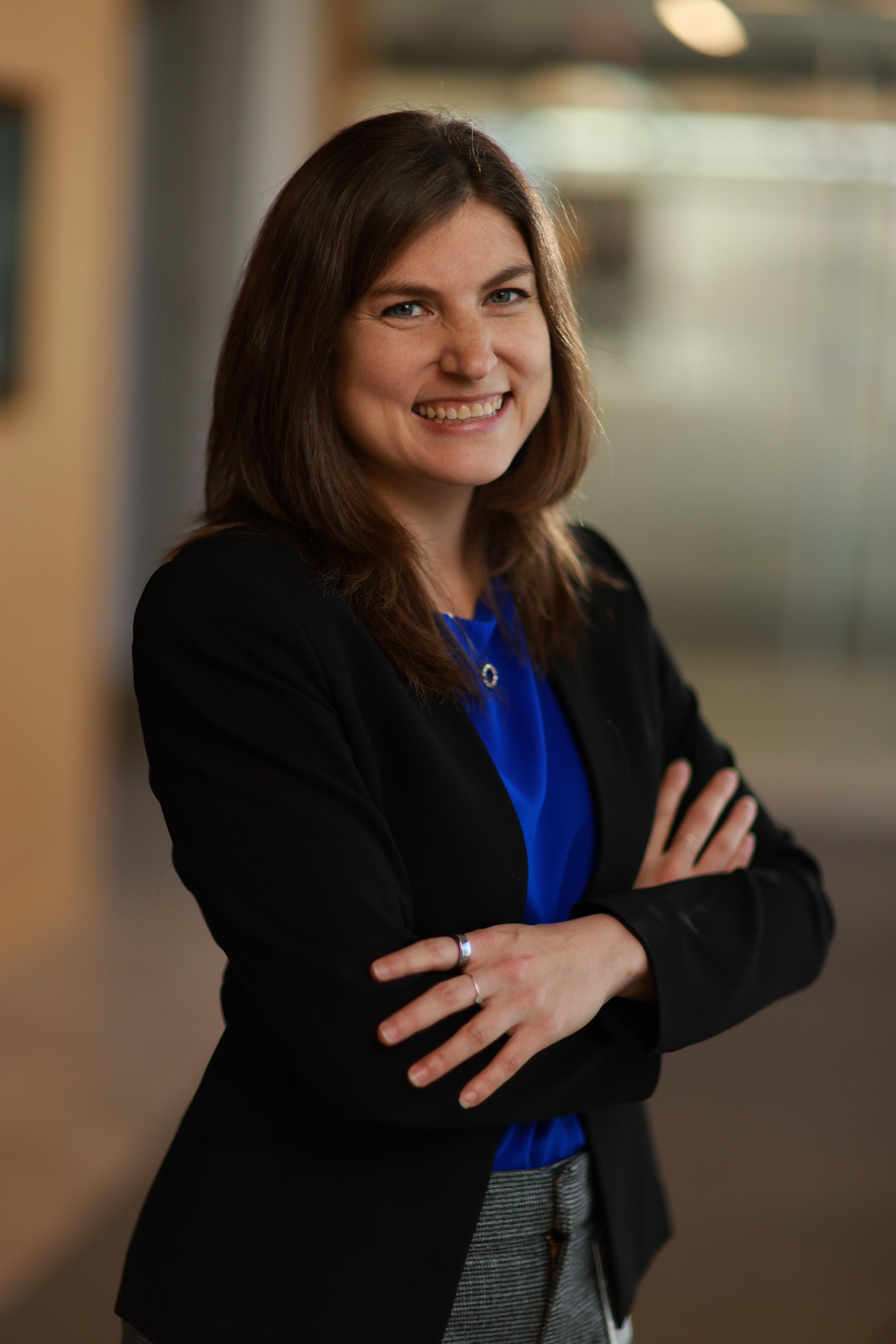 Owner and founder Shira Stoll has brown hair and is smiling, wearing a black blazer and blue top, standing with arms crossed in a professional setting.