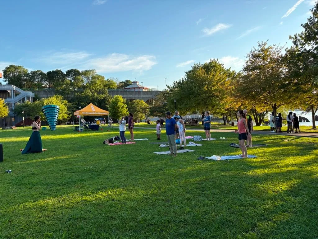People practicing Joyflow outdoors in a park with trees, sunlight, and a body of water nearby.