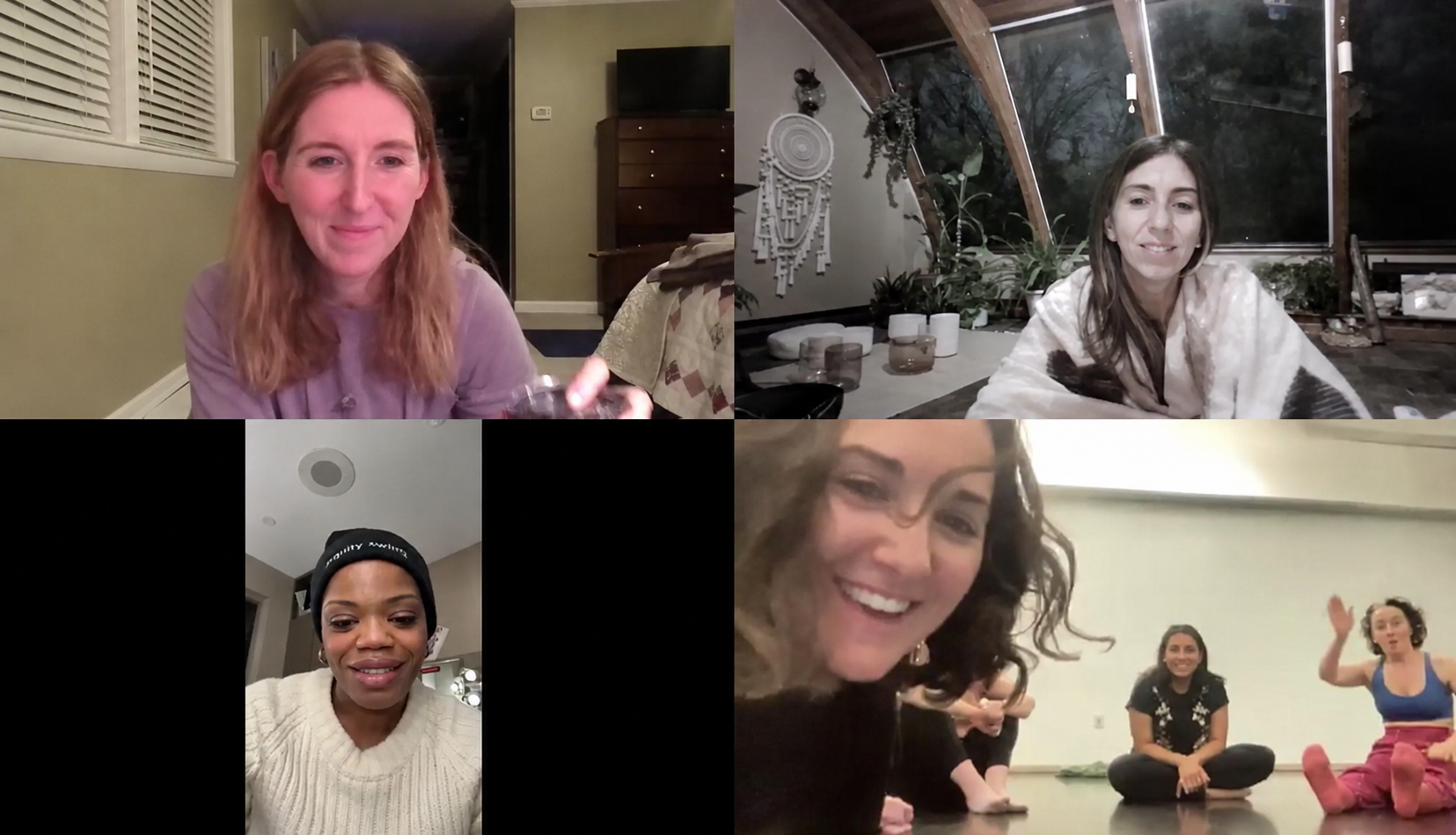 A virtual group video call with five women. Top left, a woman with long red hair in a lavender shirt, holding a glass. Top right, a woman with brown hair in a cozy sweater, sitting in a room with large windows and plants. Bottom left, a woman wearing a black beanie and white sweater, smiling. Bottom right, a woman with curly hair smiling, and two women in the background sitting on the floor, one gesturing with her hand in a room with a beige wall.