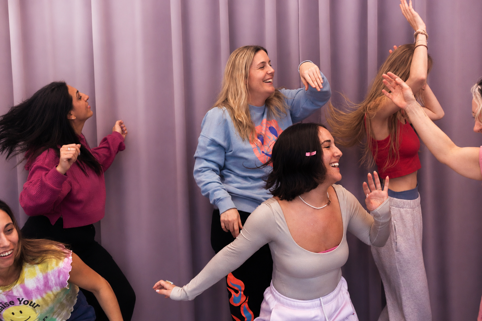 Group of women dancing and laughing against purple curtain background