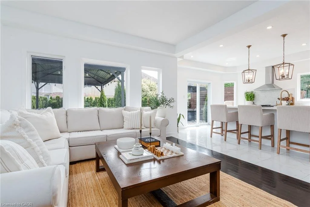 Bright, modern open-concept living room and kitchen with white furniture, wooden accents, and large windows.