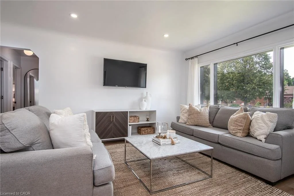 Living room with two gray sofas, a marble coffee table, and a large window showing greenery outside.