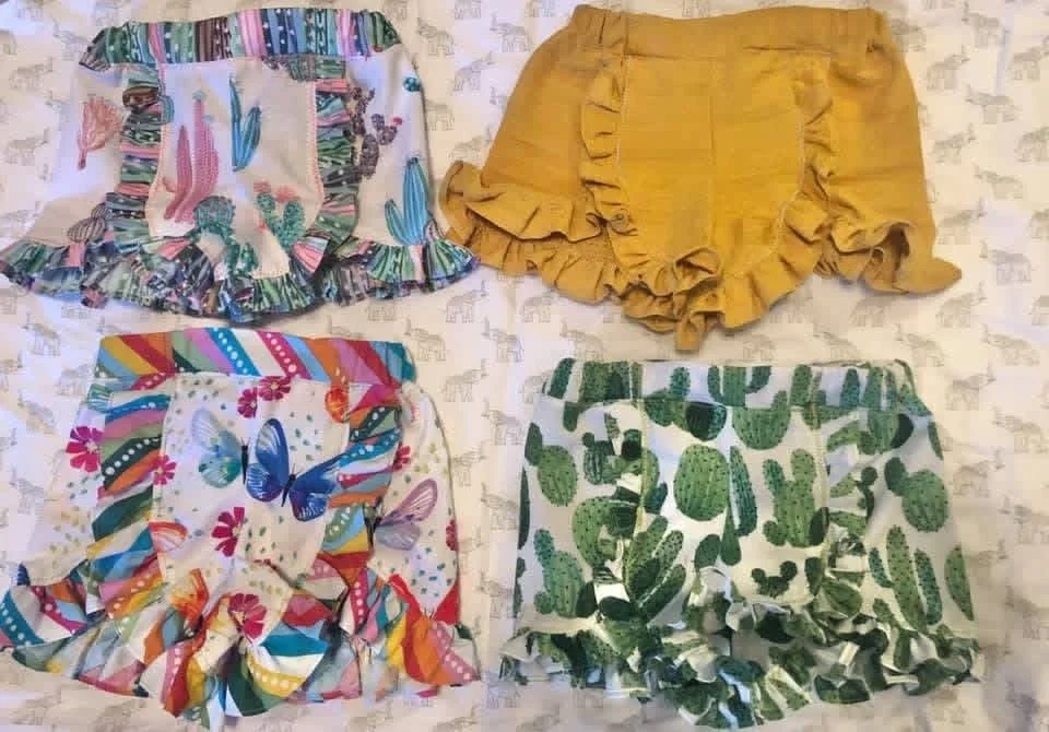Four pairs of children's ruffled shorts with various colorful patterns and designs displayed on a surface.