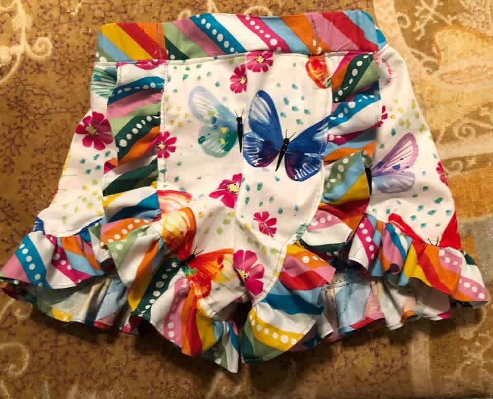 Colorful children's ruffled skirt with butterfly and floral print on a brown textured surface.