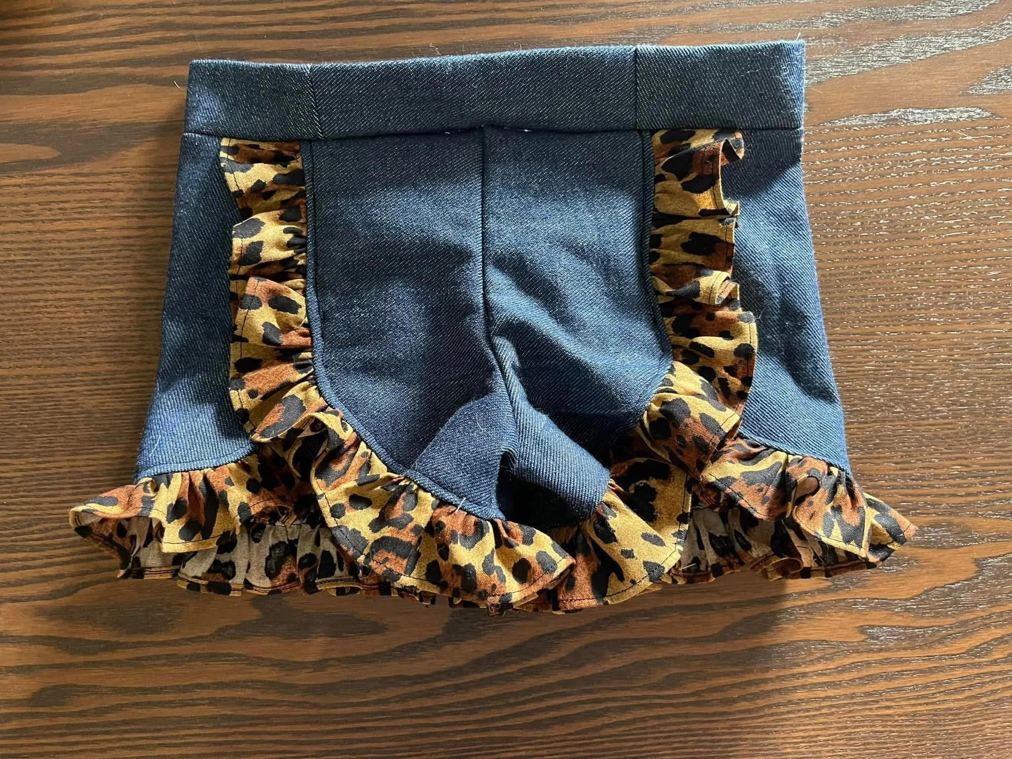 Close-up of denim shorts with leopard print ruffled trim on a wooden surface.