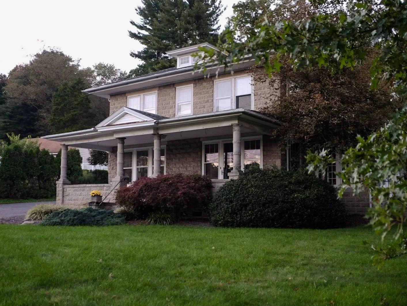 A two-story house with a brick and stone exterior, a front porch with white columns, and a well-maintained lawn with bushes and trees.
